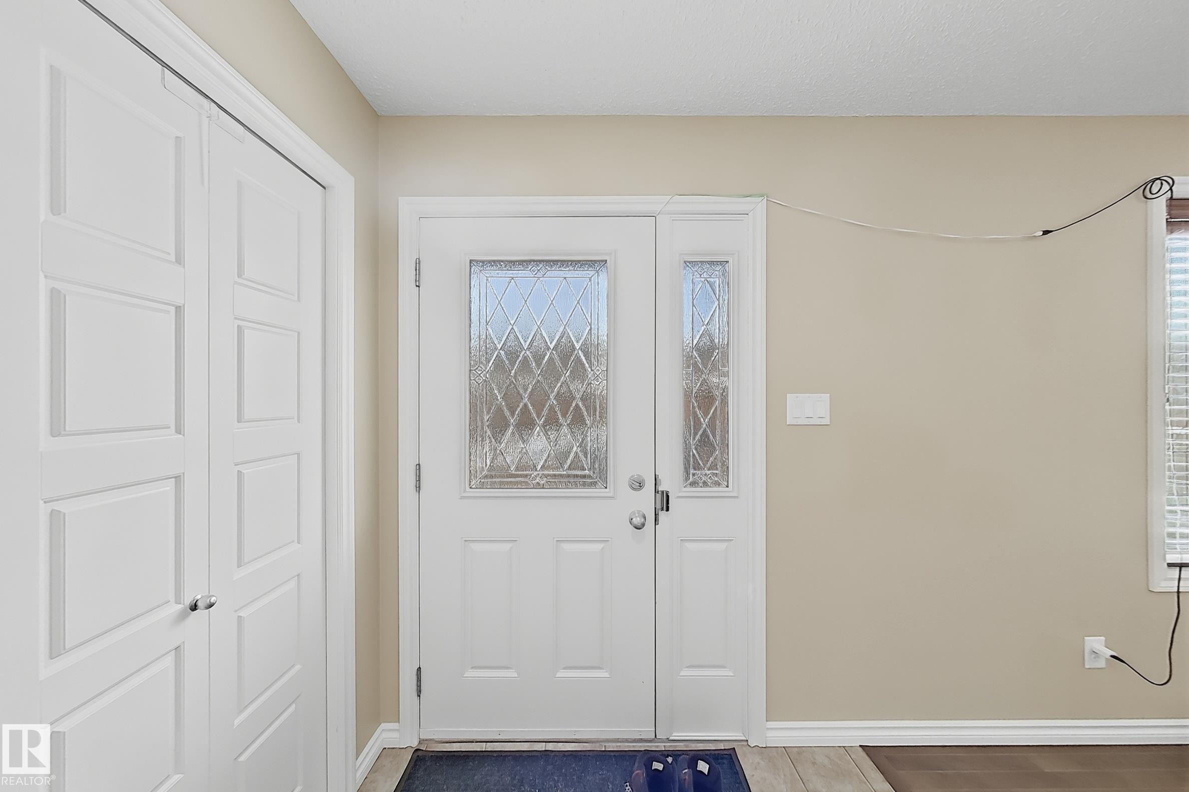 Entryway featuring a decorative glass main door with a sidelight, neutral wall paint, white baseboards, and a bi-fold closet - 3609 Weidle Bend, Edmonton, AB - Indoor Photo Showing Other Room