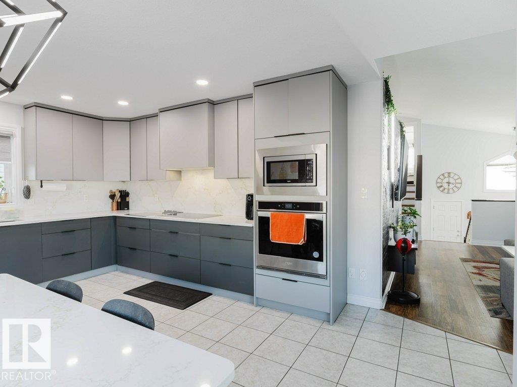Contemporary kitchen featuring two-tone cabinetry, integrated stainless steel appliances including a wall oven and microwave, white quartz countertops, and a full tile backsplash - 5701 Rue Eaglemont, Beaumont, AB - Indoor Photo Showing Kitchen