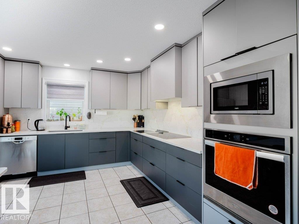 Modern kitchen featuring two-tone cabinetry, stainless steel appliances, a built-in microwave and oven, a black faucet, and patterned tile flooring - 5701 Rue Eaglemont, Beaumont, AB - Indoor Photo Showing Kitchen With Upgraded Kitchen