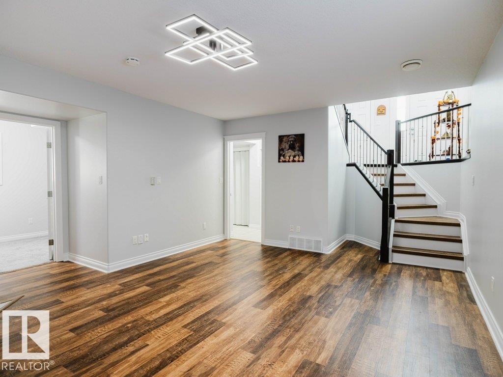Spacious room featuring wood-finish flooring, white baseboards, and light gray walls - 5701 Rue Eaglemont, Beaumont, AB - Indoor Photo Showing Other Room