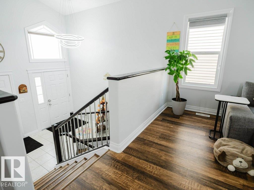Open-concept entry foyer featuring a striking contemporary light fixture, a large transom window, and a white paneled entry door with a frosted glass insert - 5701 Rue Eaglemont, Beaumont, AB - Indoor Photo Showing Other Room