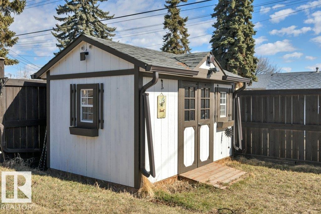Detached storage shed featuring white siding with dark trim, dual paneled doors, a single window with decorative shutters, and a shingled roof - 10633 St Gabriel School Road, Edmonton, AB - Outdoor