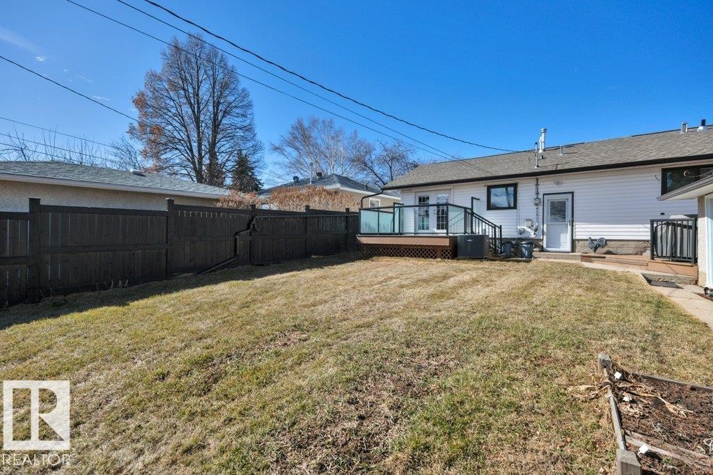Expansive backyard featuring a large wood deck with glass panel railing, white vinyl siding, a dark privacy fence, and a raised garden bed - 10633 St Gabriel School Road, Edmonton, AB - Outdoor With Deck Patio Veranda