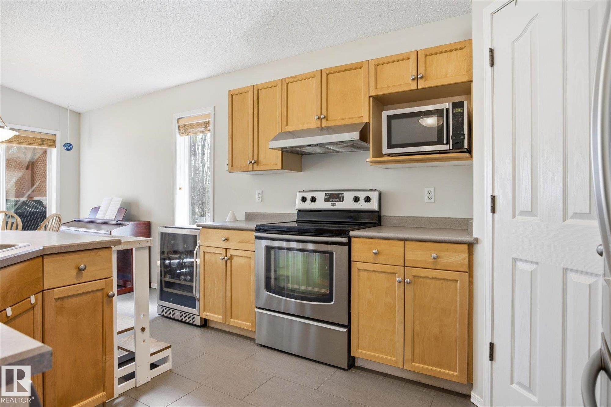 Kitchen featuring natural wood-finish cabinetry, stainless steel range and microwave, and a built-in wine refrigerator - 2251 Brennan Court, Edmonton, AB - Indoor Photo Showing Kitchen With Stainless Steel Kitchen