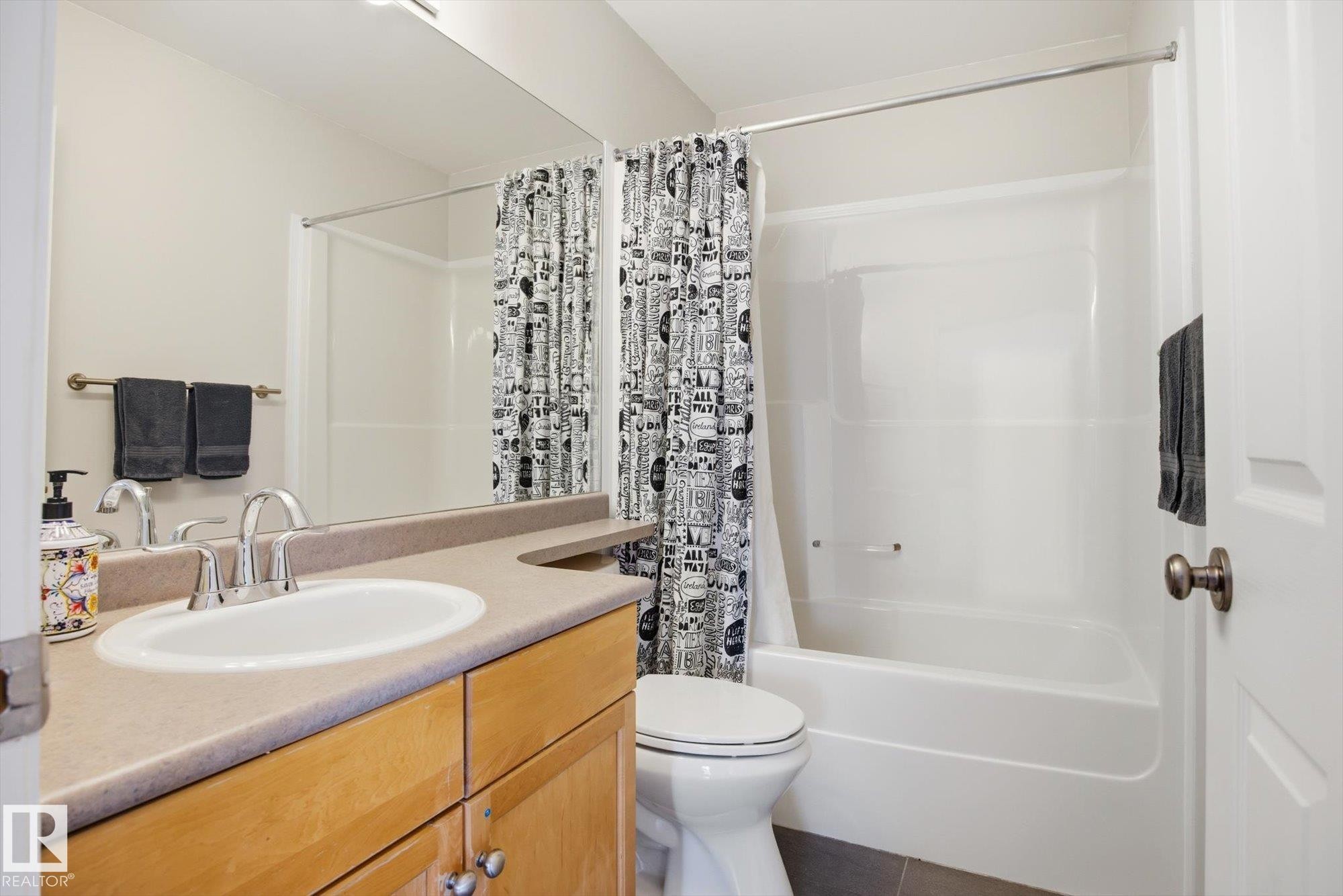 Full bathroom featuring a single vanity with an integrated sink, wood-finish cabinetry, a full-width mirror, a toilet, and a combined tub and shower unit - 2251 Brennan Court, Edmonton, AB - Indoor Photo Showing Bathroom