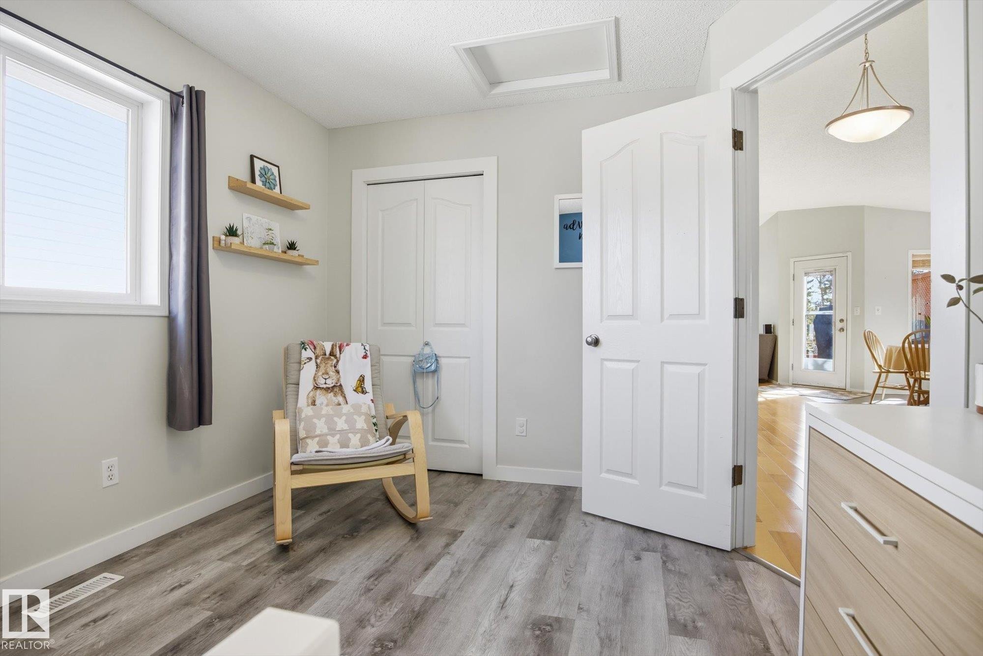 Neutral-toned room featuring wood-finish flooring, a white trim window, a panel door, and bi-fold closet doors - 2251 Brennan Court, Edmonton, AB - Indoor