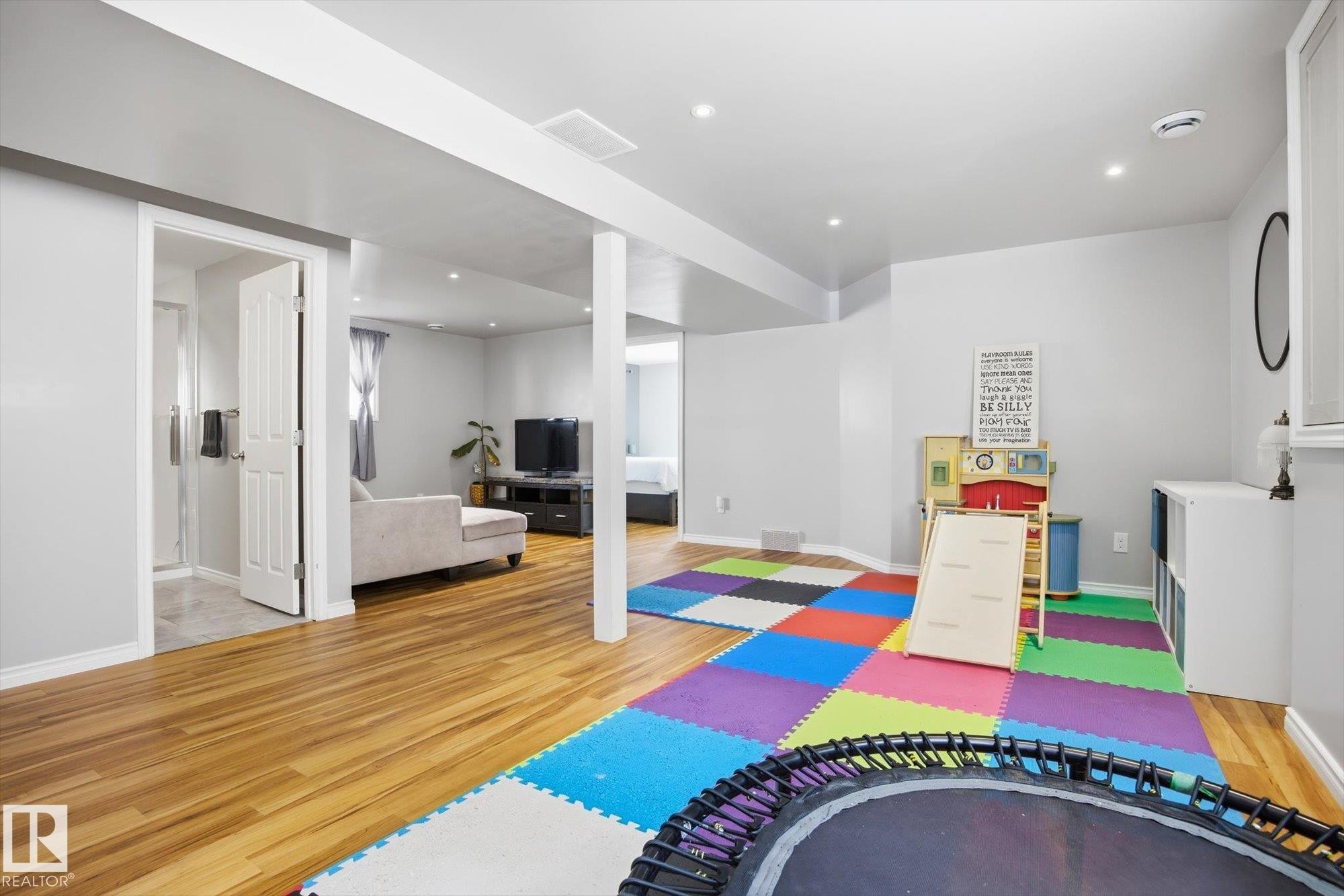 Spacious open-concept lower level featuring wood-finish flooring, recessed lighting, a neutral color palette, and a clear glass shower enclosure visible through an open doorway - 2251 Brennan Court, Edmonton, AB - Indoor Photo Showing Other Room