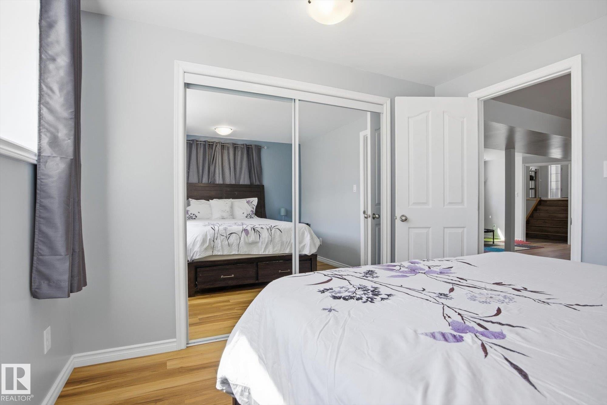 Spacious room featuring wood-finish flooring, a built-in mirrored closet, and light gray wall paint - 2251 Brennan Court, Edmonton, AB - Indoor Photo Showing Bedroom