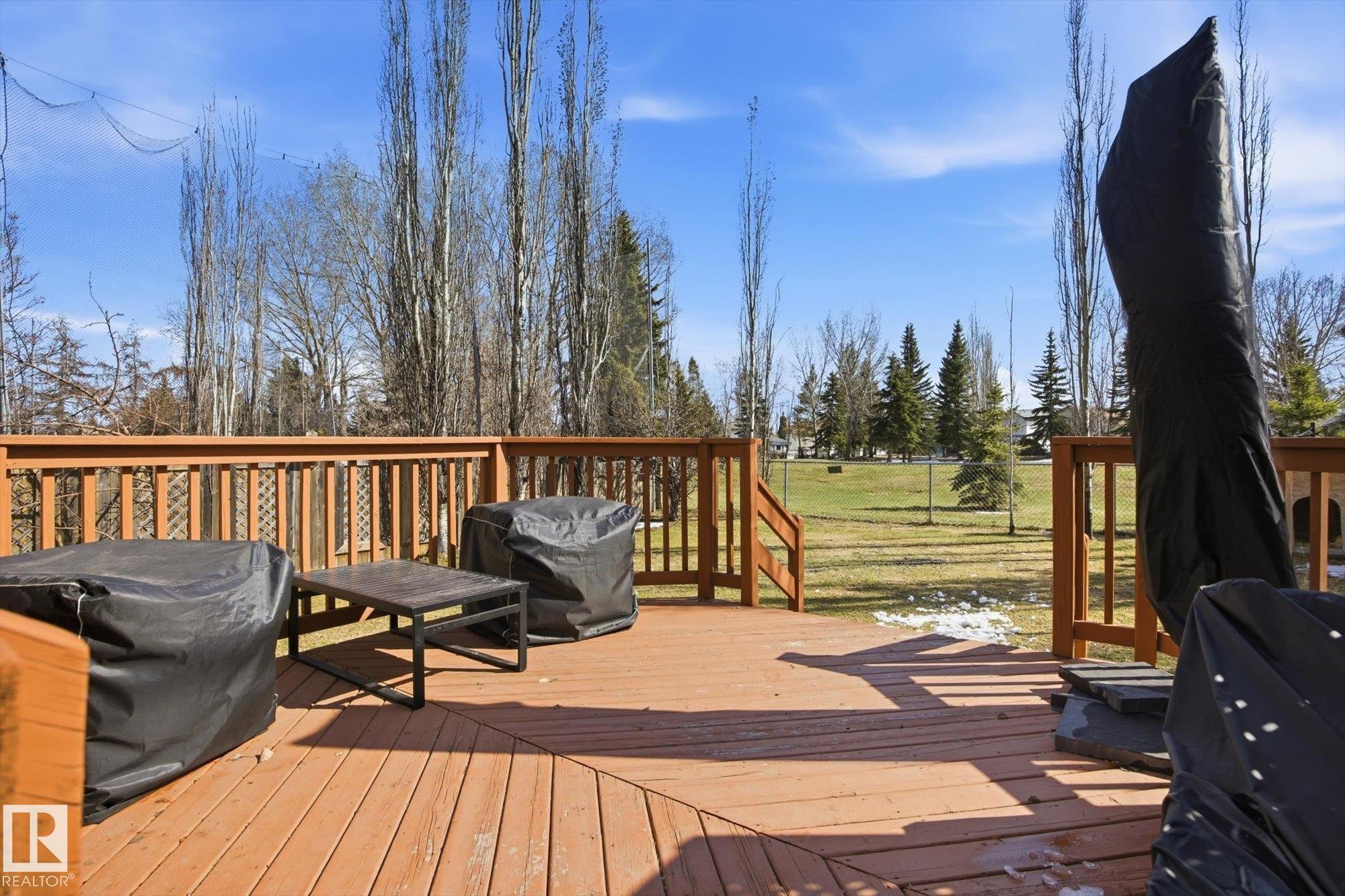 Expansive outdoor wood deck with natural wood railing overlooking a sloped grassy area bordered by mature trees - 2251 Brennan Court, Edmonton, AB - Outdoor With Deck Patio Veranda With Exterior