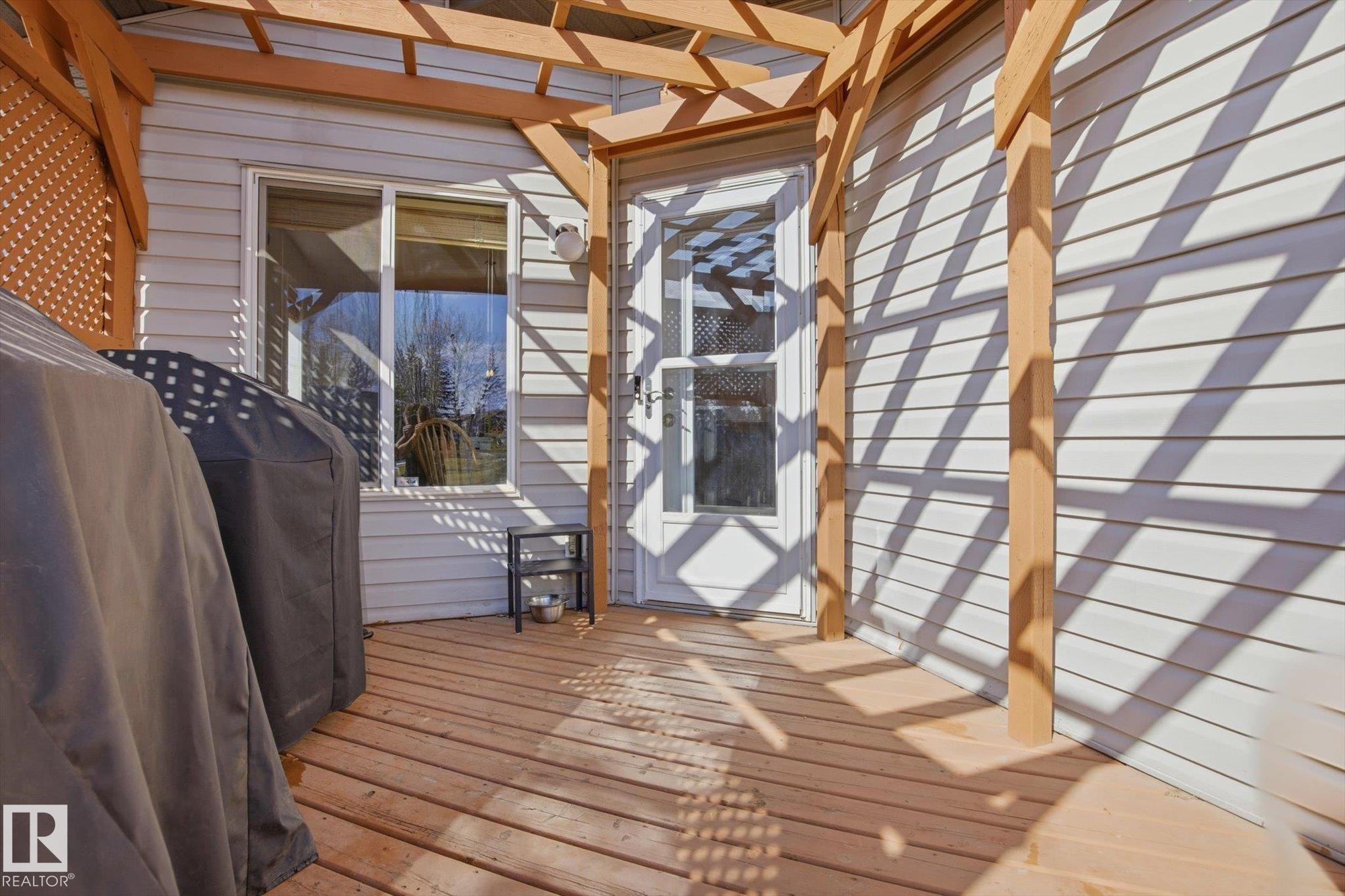 Outdoor wood deck featuring a lattice pergola, white vinyl siding, and a glass-paned exterior door - 2251 Brennan Court, Edmonton, AB - With Exterior