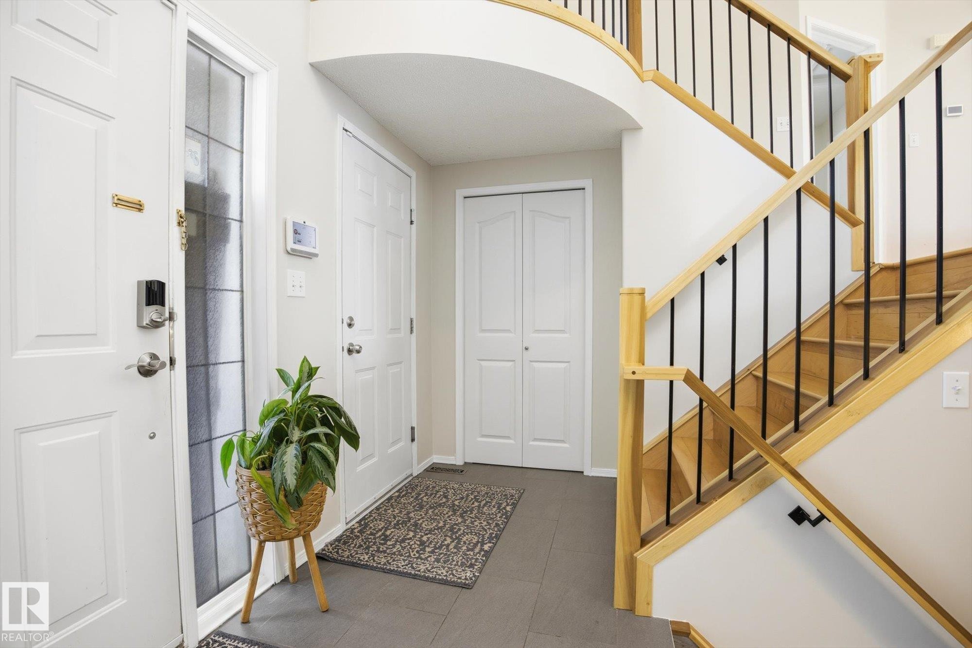 Foyer featuring a curved staircase with natural wood handrails and black iron balusters - 2251 Brennan Court, Edmonton, AB - Indoor Photo Showing Other Room