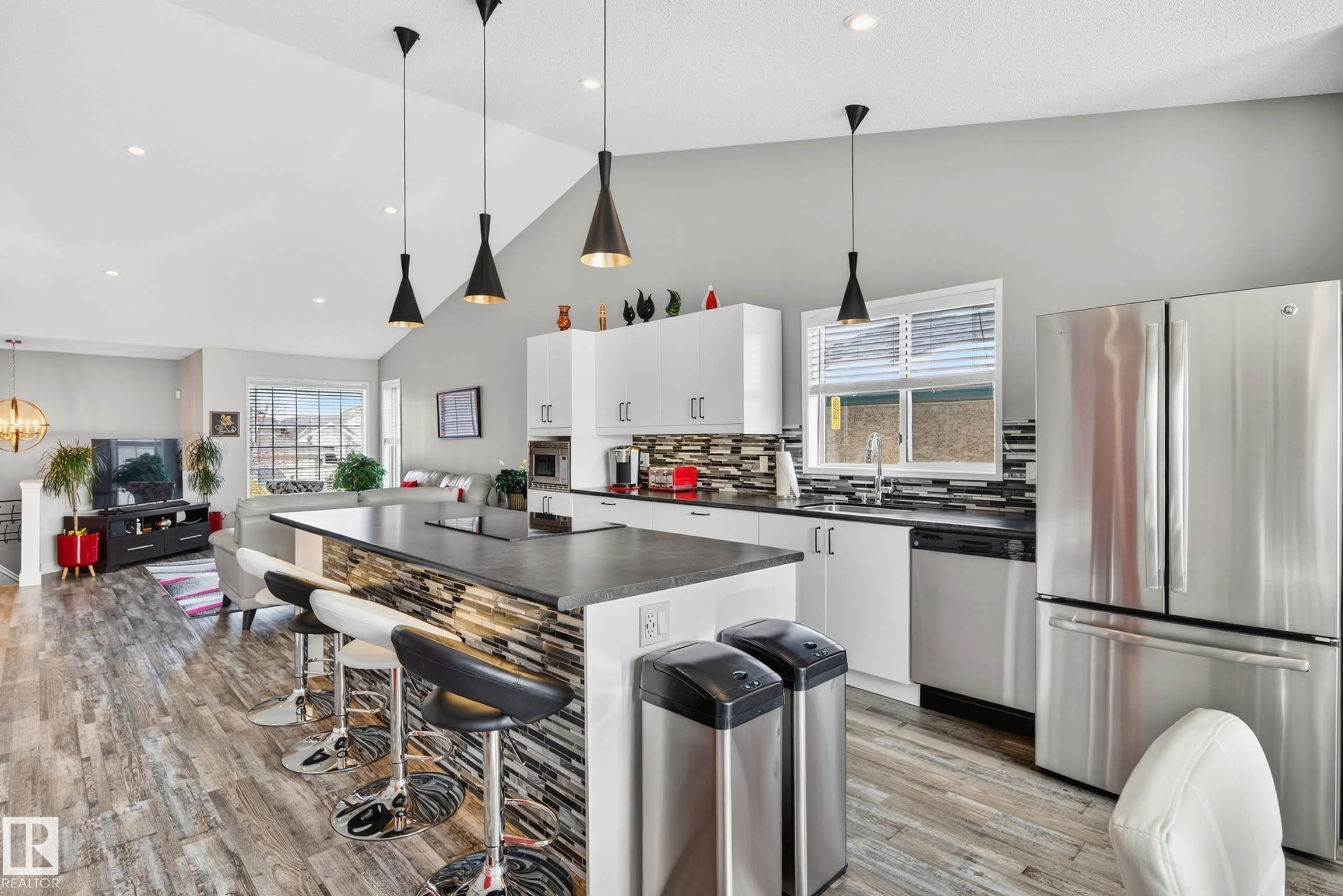 The kitchen features a large island with a stone-accented base, pendant lighting, and stainless steel appliances, including a refrigerator and dishwasher - 34 Donald Place, St. Albert, AB - Indoor