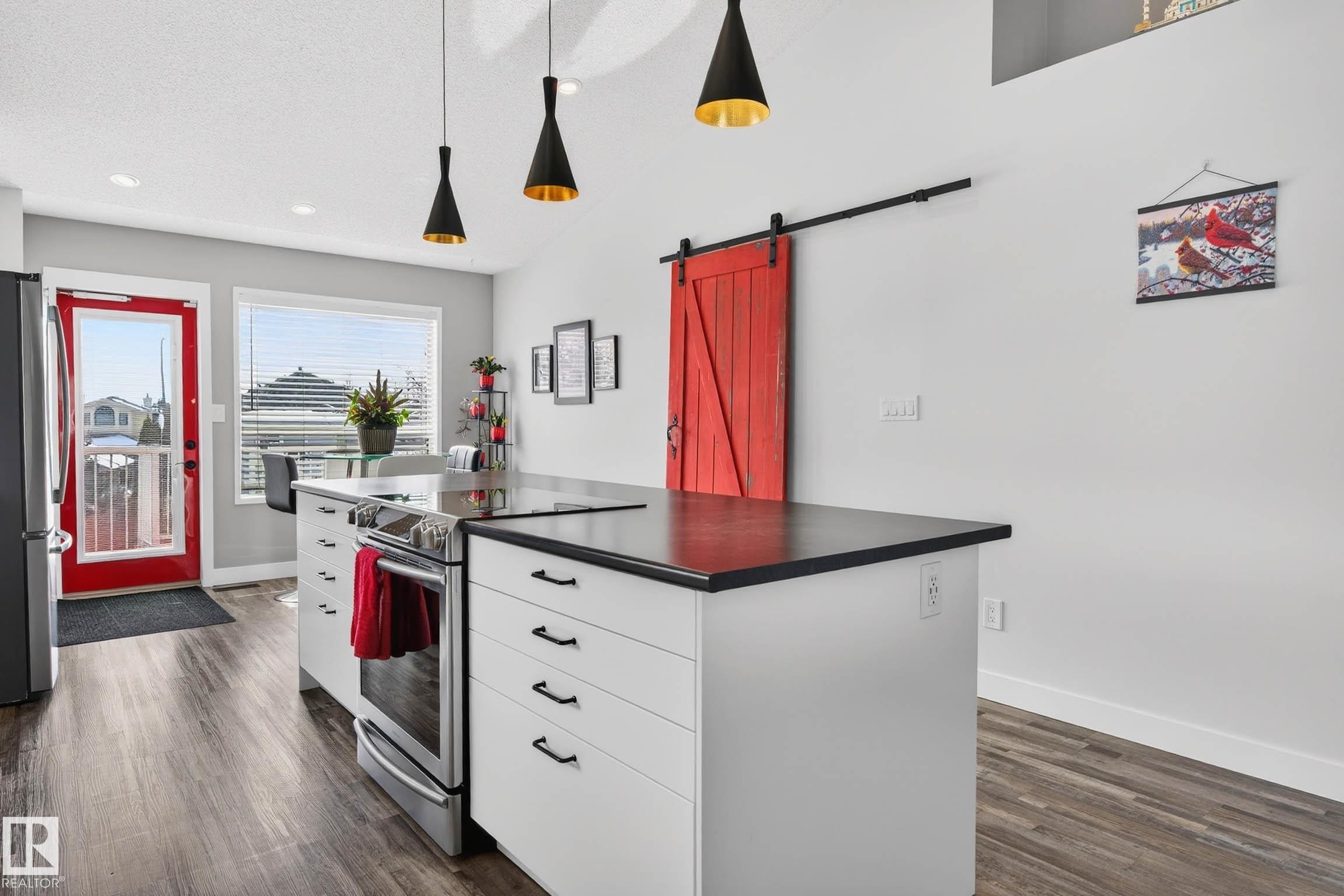 The kitchen features a functional island with an integrated stove and black countertops, modern pendant lighting, and a distinctive red barn door - 34 Donald Place, St. Albert, AB - Indoor Photo Showing Kitchen