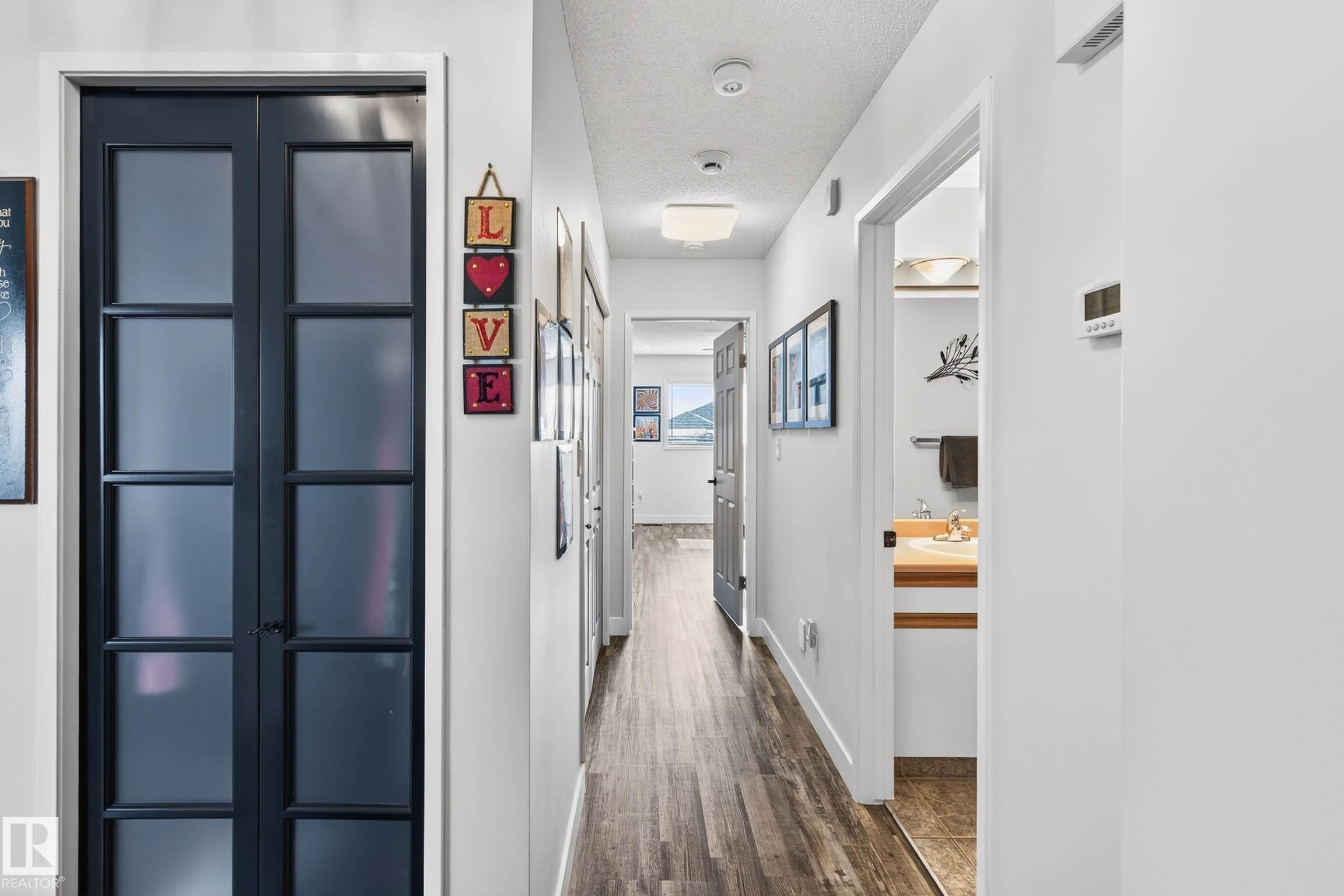 Hallway featuring dark wood-style flooring, white walls, and a view into a bathroom with a wooden vanity - 34 Donald Place, St. Albert, AB - Indoor Photo Showing Other Room