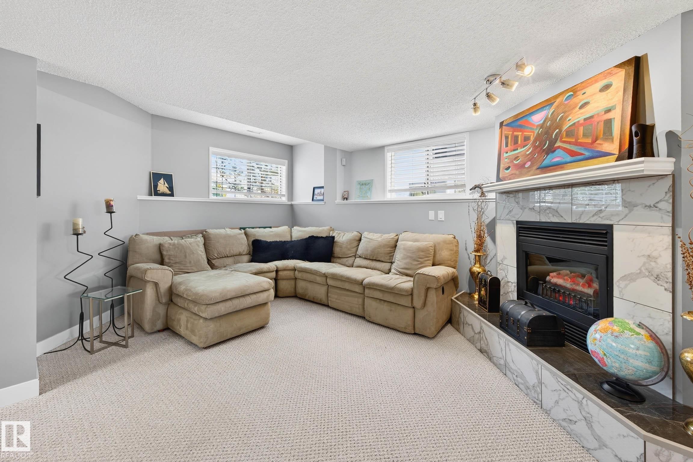 This inviting living space features carpeting, a corner sectional sofa, and a fireplace with a marble surround and hearth - 34 Donald Place, St. Albert, AB - Indoor Photo Showing Living Room With Fireplace