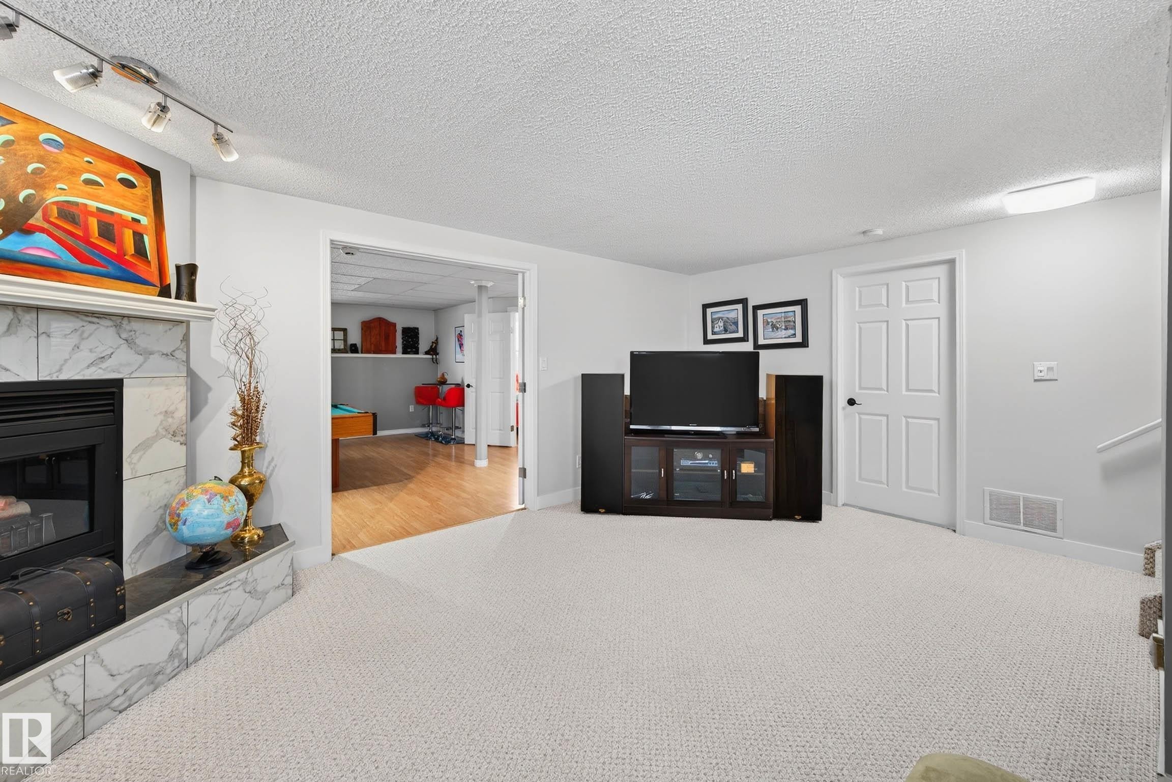 The living area features light-colored carpeting, a fireplace with a marble surround, and recessed lighting - 34 Donald Place, St. Albert, AB - Indoor With Fireplace