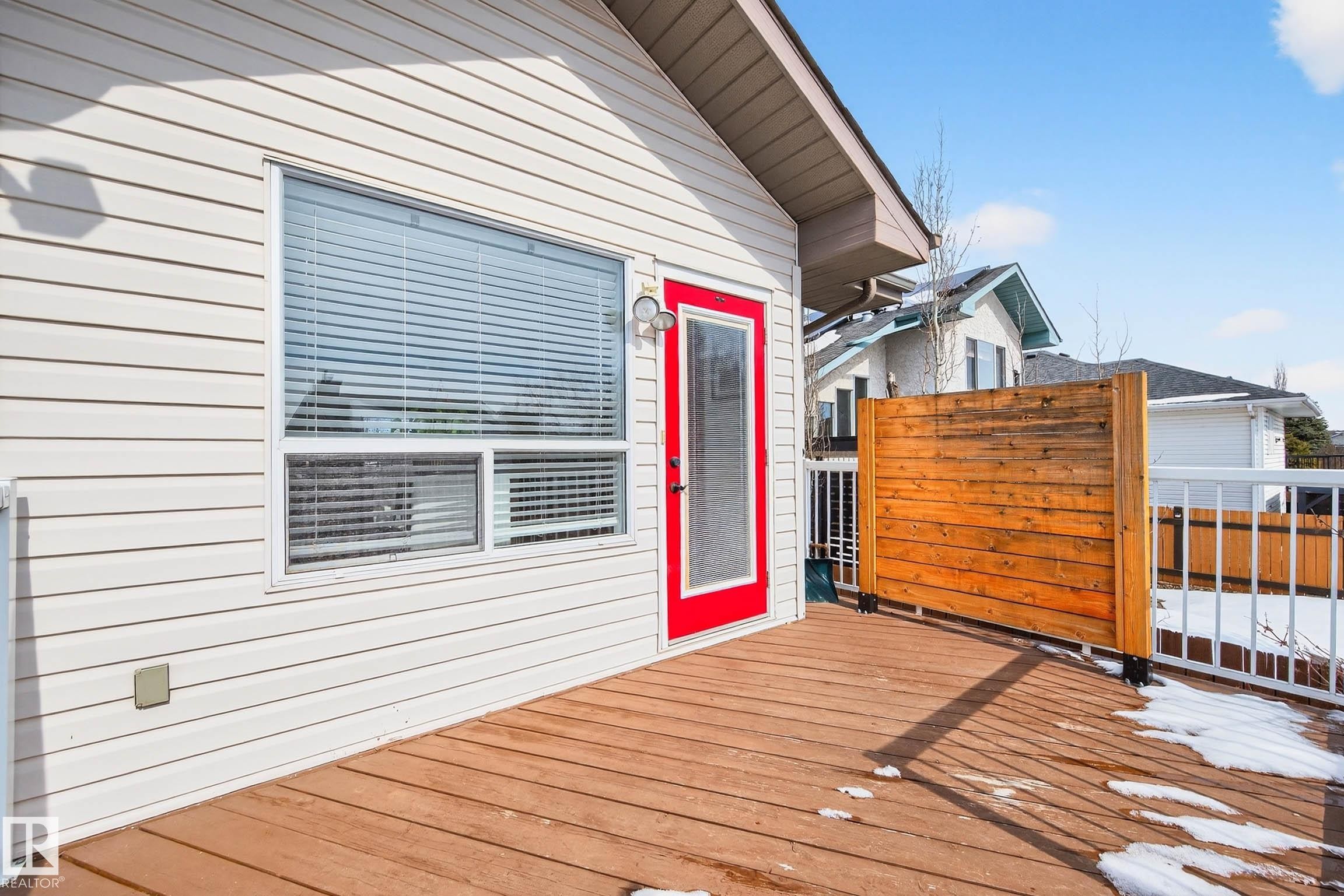 The property features a spacious exterior deck with wood flooring and white railings, a red exterior door, and a horizontal privacy screen - 34 Donald Place, St. Albert, AB - Outdoor With Exterior