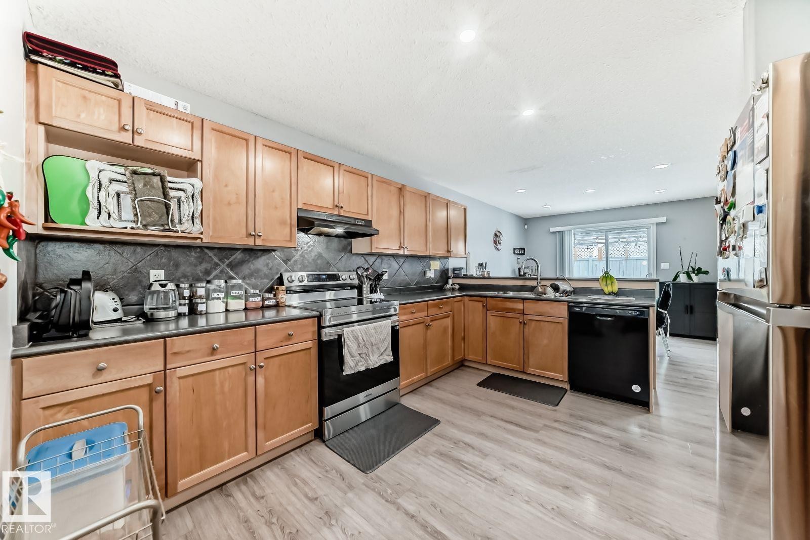 Kitchen featuring wood-finish flooring, natural wood cabinetry, dark countertops, and a tile backsplash - 715 Hudson Place, Edmonton, AB - Indoor Photo Showing Kitchen With Double Sink