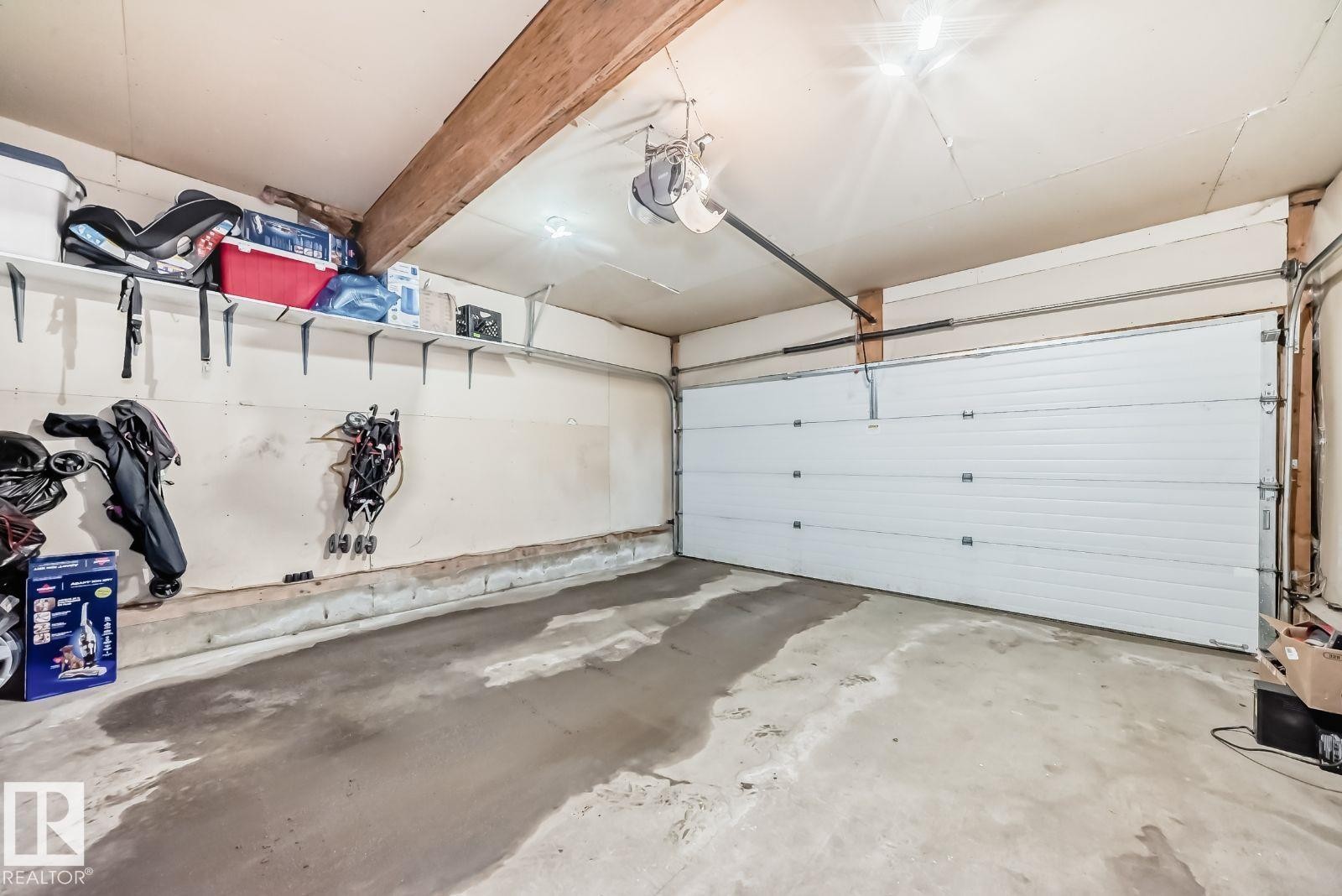 Single-car garage featuring a white panel door, concrete flooring, and an exposed wood beam ceiling - 715 Hudson Place, Edmonton, AB - Indoor Photo Showing Garage
