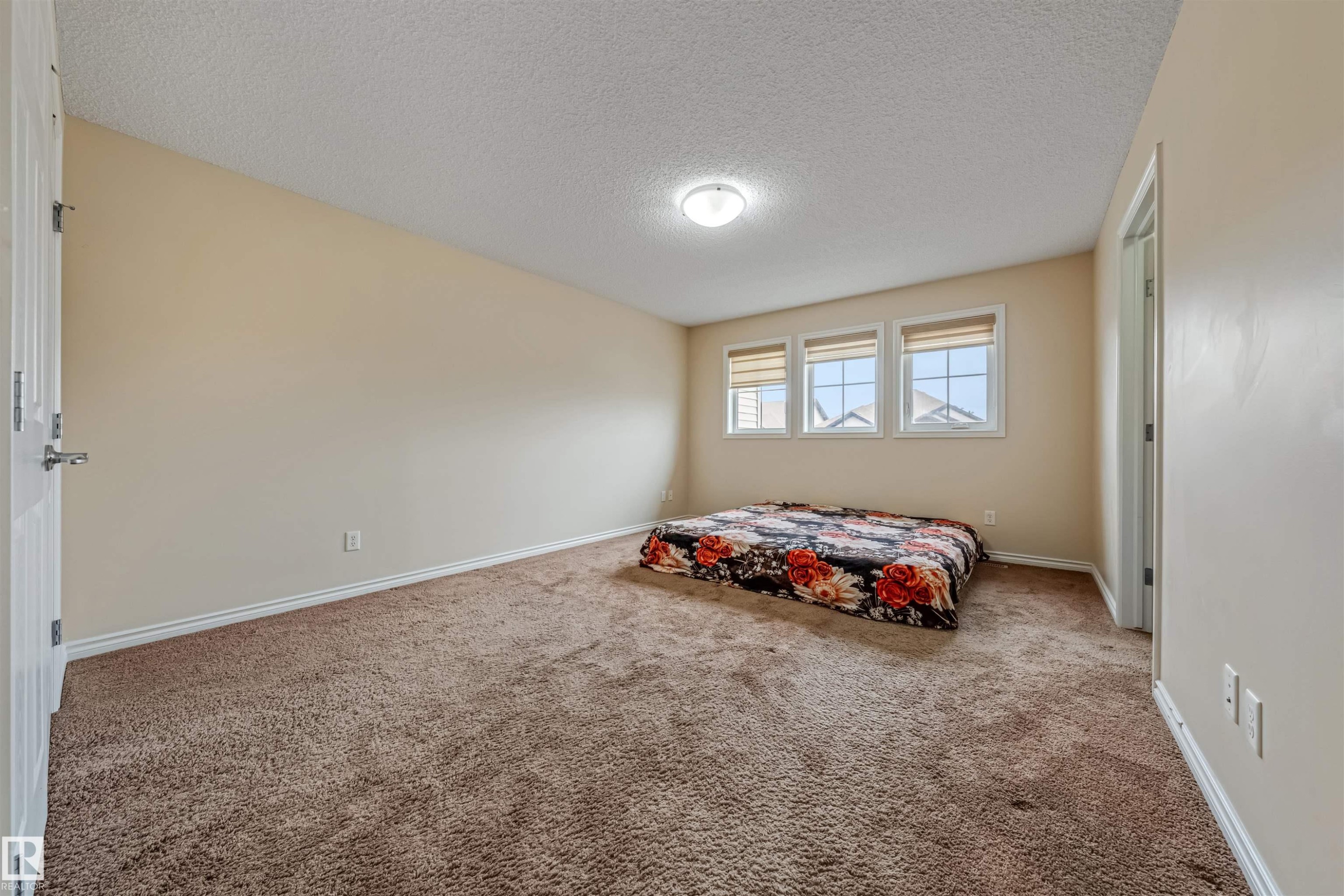 Spacious room featuring neutral paint, textured carpeting, white baseboards, and three large windows - 2314 22 Avenue, Edmonton, AB - Indoor Photo Showing Bedroom