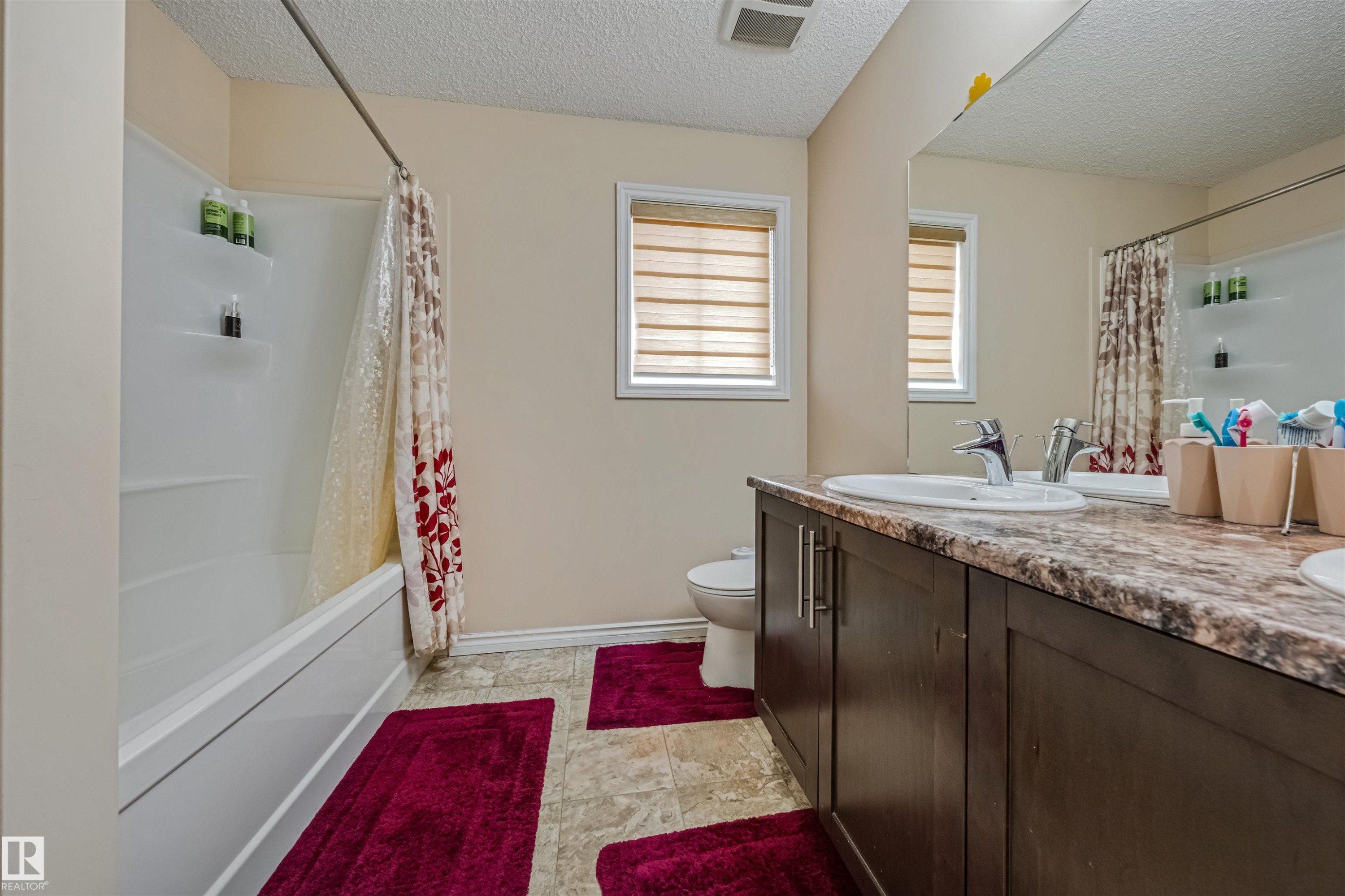 Bathroom featuring a double vanity with an integrated sink, a spacious mirror, and a combination tub and shower unit - 2314 22 Avenue, Edmonton, AB - Indoor Photo Showing Bathroom