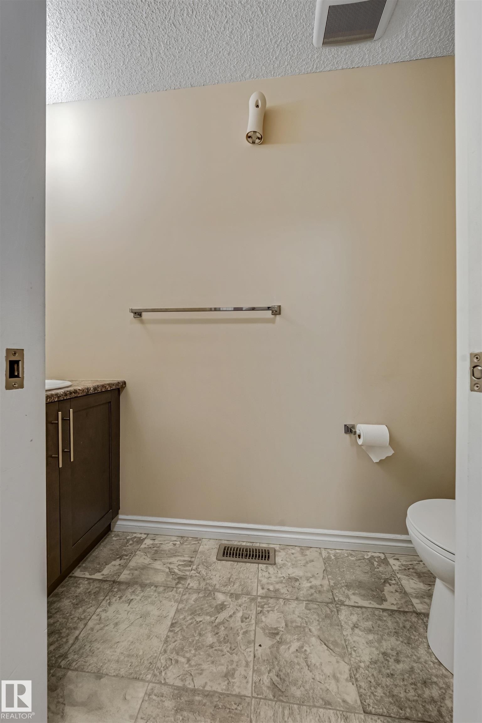 Powder room featuring a dark wood-finish vanity with a stone-look countertop, patterned tile flooring, and a white toilet - 2314 22 Avenue, Edmonton, AB - Indoor Photo Showing Bathroom