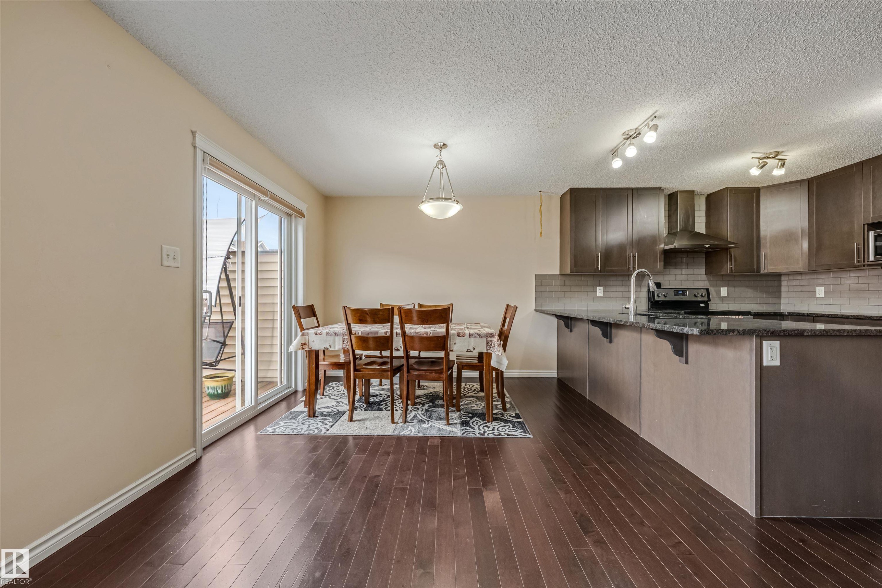 Open-concept living space featuring wood-finish flooring, a kitchen island with granite-style countertops, dark wood-finish cabinetry, stainless steel appliances, and a sliding glass door to an exterior deck - 2314 22 Avenue, Edmonton, AB - Indoor