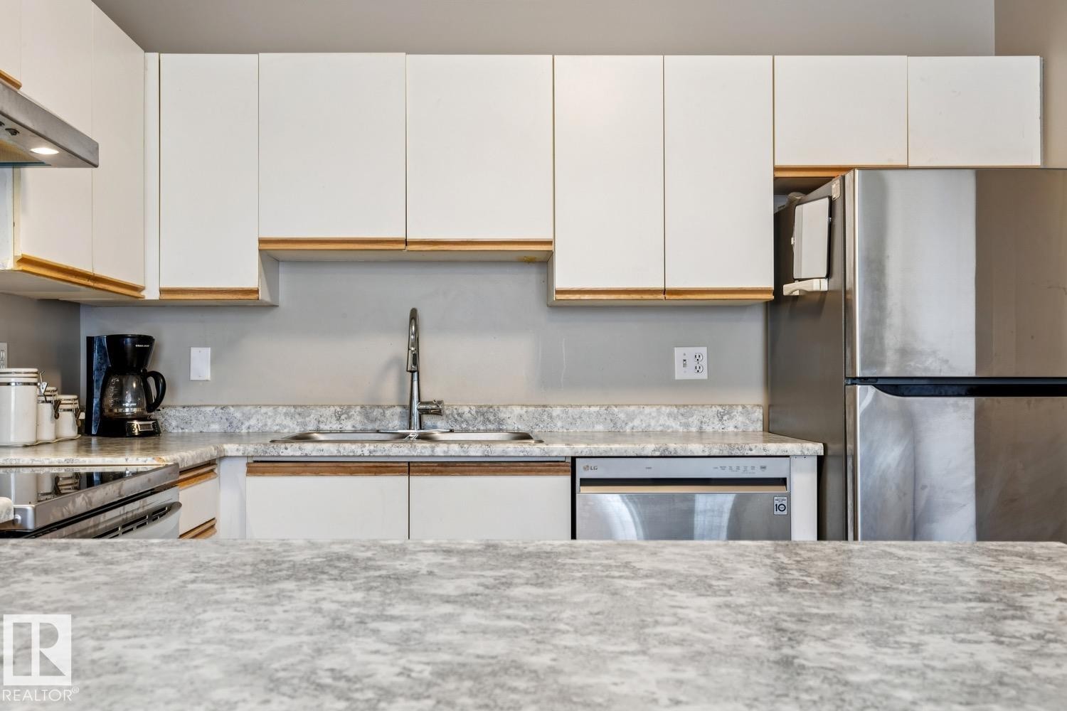 Modern kitchen featuring white flat-panel cabinetry with wood-finish accents, a stainless steel refrigerator, and integrated dishwasher - 40 9520 174 Street, Edmonton, AB - Indoor Photo Showing Kitchen With Stainless Steel Kitchen With Double Sink With Upgraded Kitchen