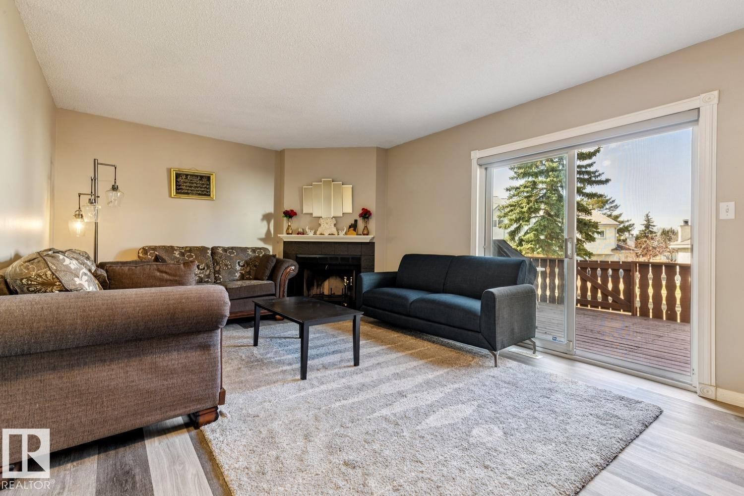 Interior space featuring light-toned walls, wood-finish flooring, a corner fireplace with a dark mantel, and a sliding glass door opening to a private deck - 40 9520 174 Street, Edmonton, AB - Indoor Photo Showing Living Room
