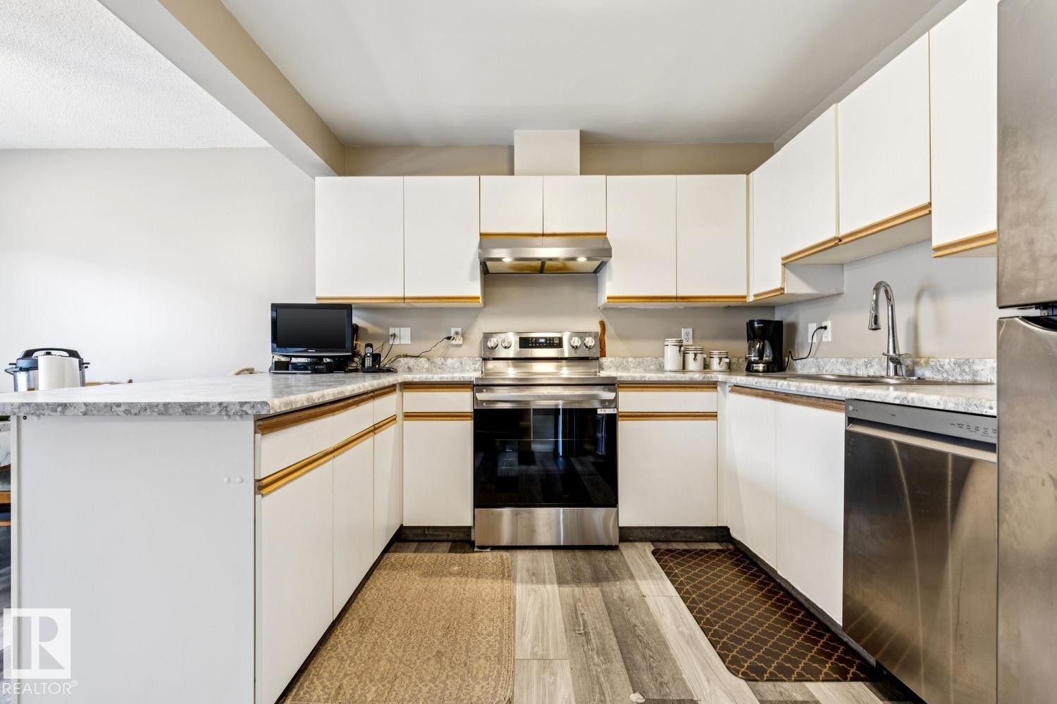 U-shaped kitchen featuring white cabinetry with gold-finish accents, light-toned granite-style countertops, stainless steel appliances, and wood-finish flooring - 40 9520 174 Street, Edmonton, AB - Indoor Photo Showing Kitchen