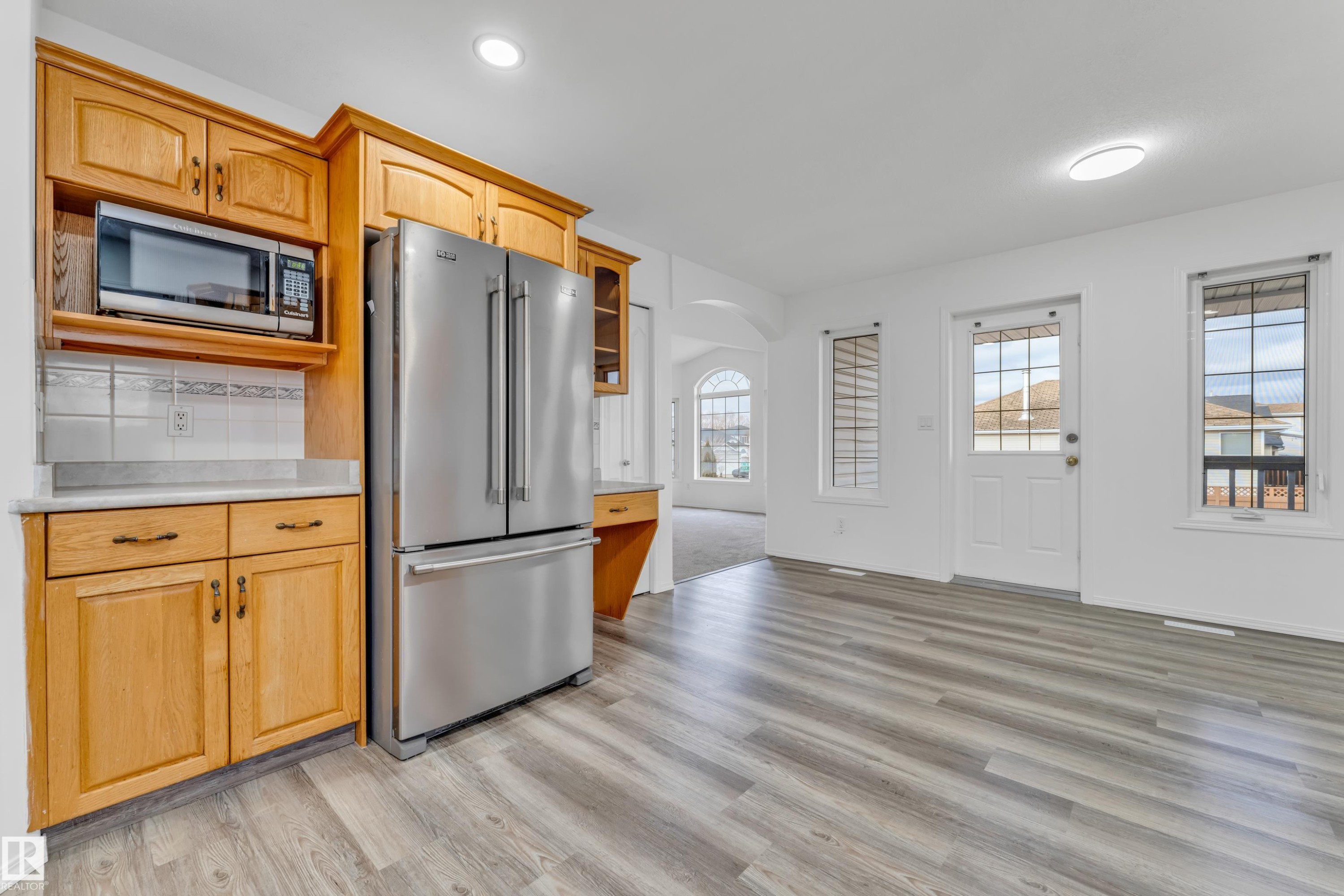 Kitchen area featuring new wood-finish flooring, light wood cabinetry, stainless steel refrigerator, and a built-in microwave - 4103 37A Avenue, Edmonton, AB - Indoor Photo Showing Kitchen