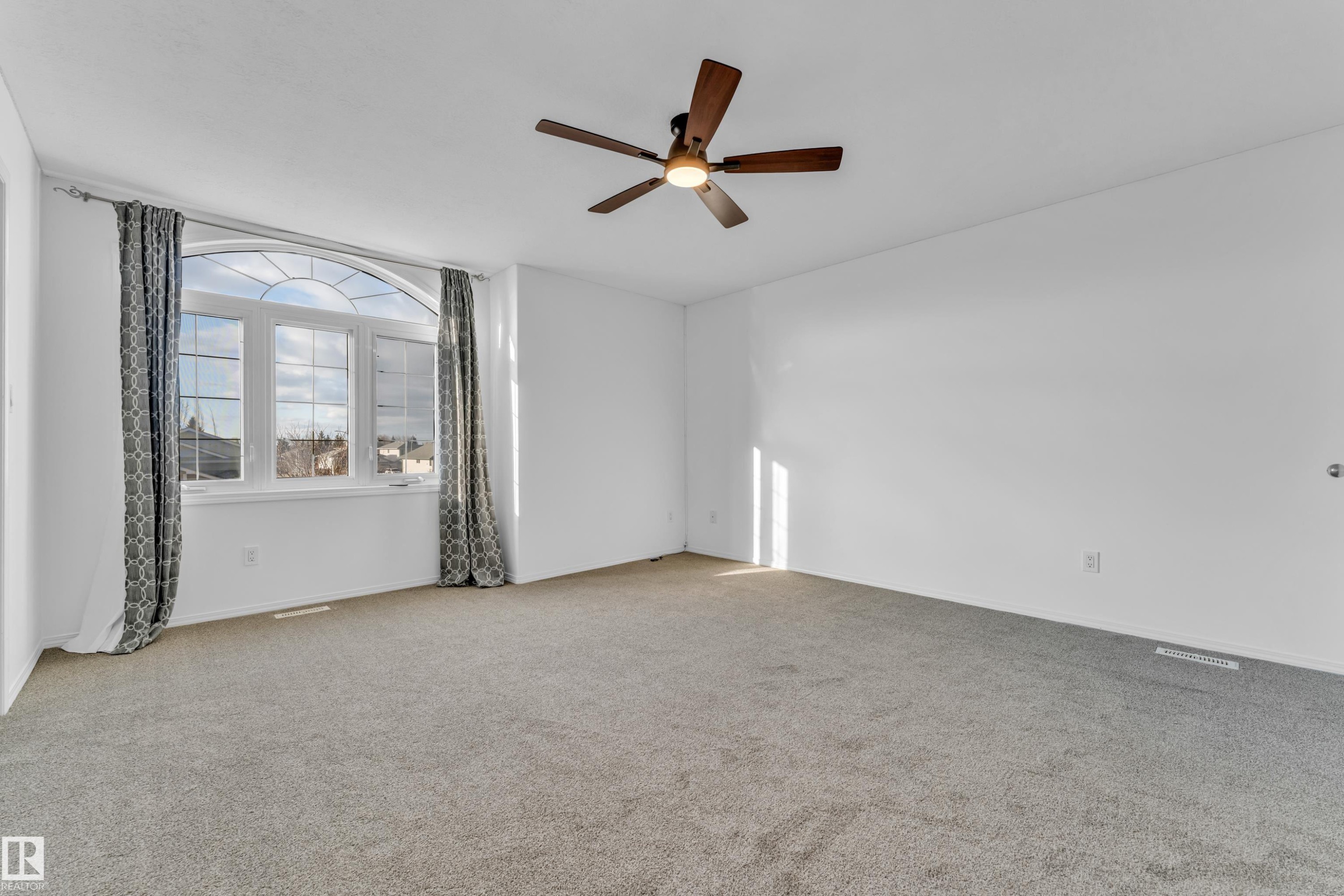 Spacious room featuring a large arched window, light gray carpeting, and a wood-finish ceiling fan with integrated lighting - 4103 37A Avenue, Edmonton, AB - Indoor Photo Showing Other Room
