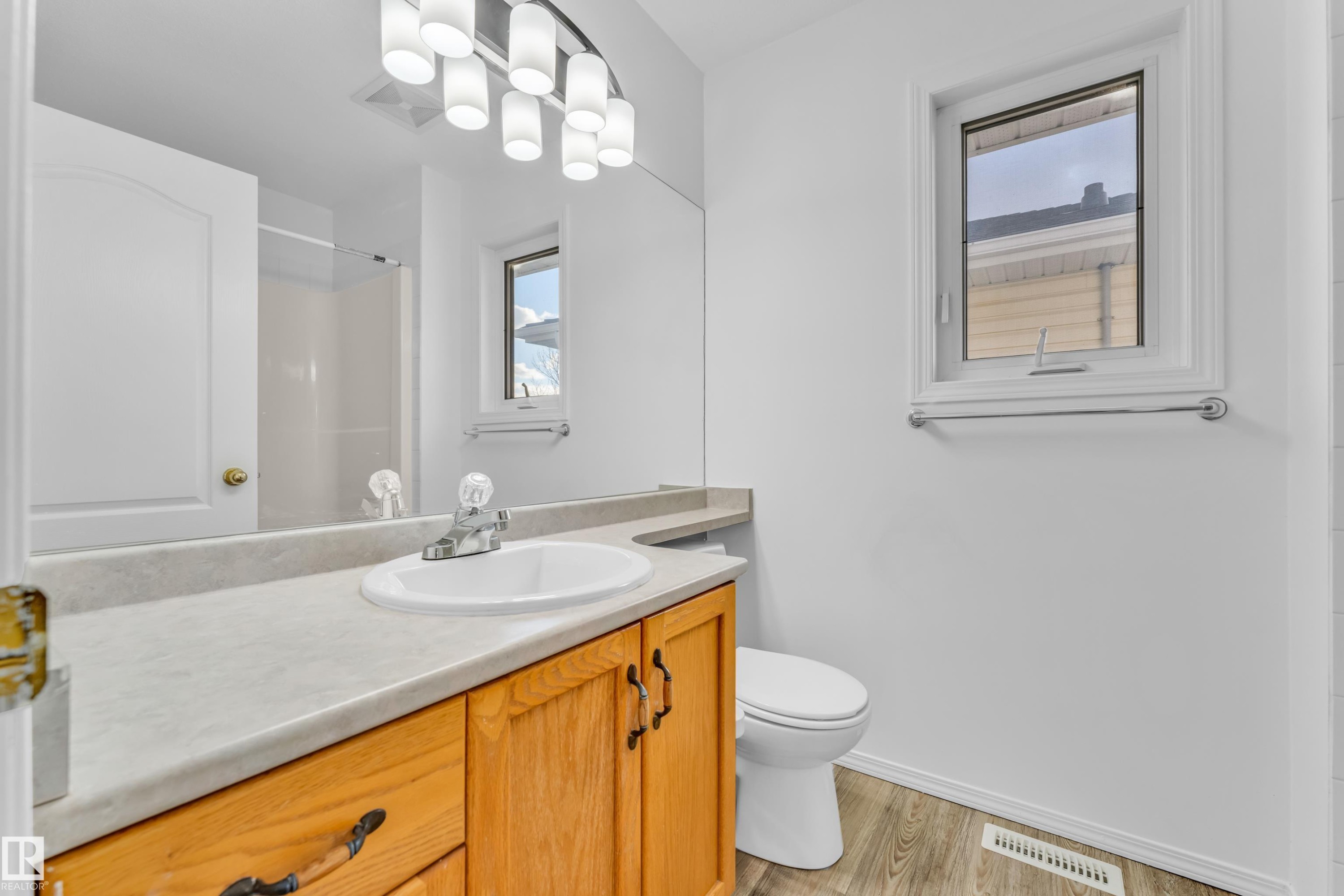 Bathroom featuring a light wood-finish vanity with an integrated sink, a neutral-toned countertop, a window with white trim, and wood-finish flooring - 4103 37A Avenue, Edmonton, AB - Indoor Photo Showing Bathroom
