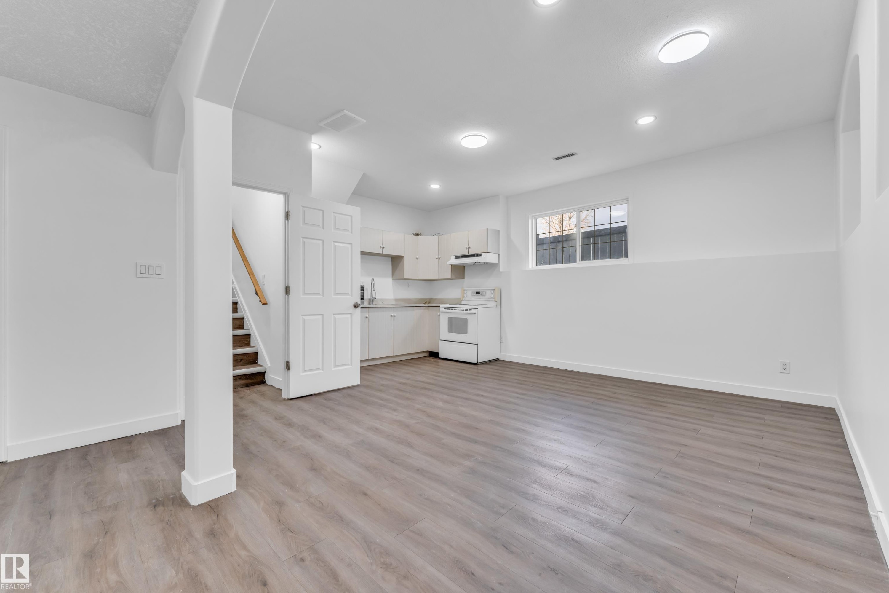 Open-concept living area featuring wood-finish flooring, recessed lighting, and a full kitchen with white cabinetry - 4103 37A Avenue, Edmonton, AB - Indoor
