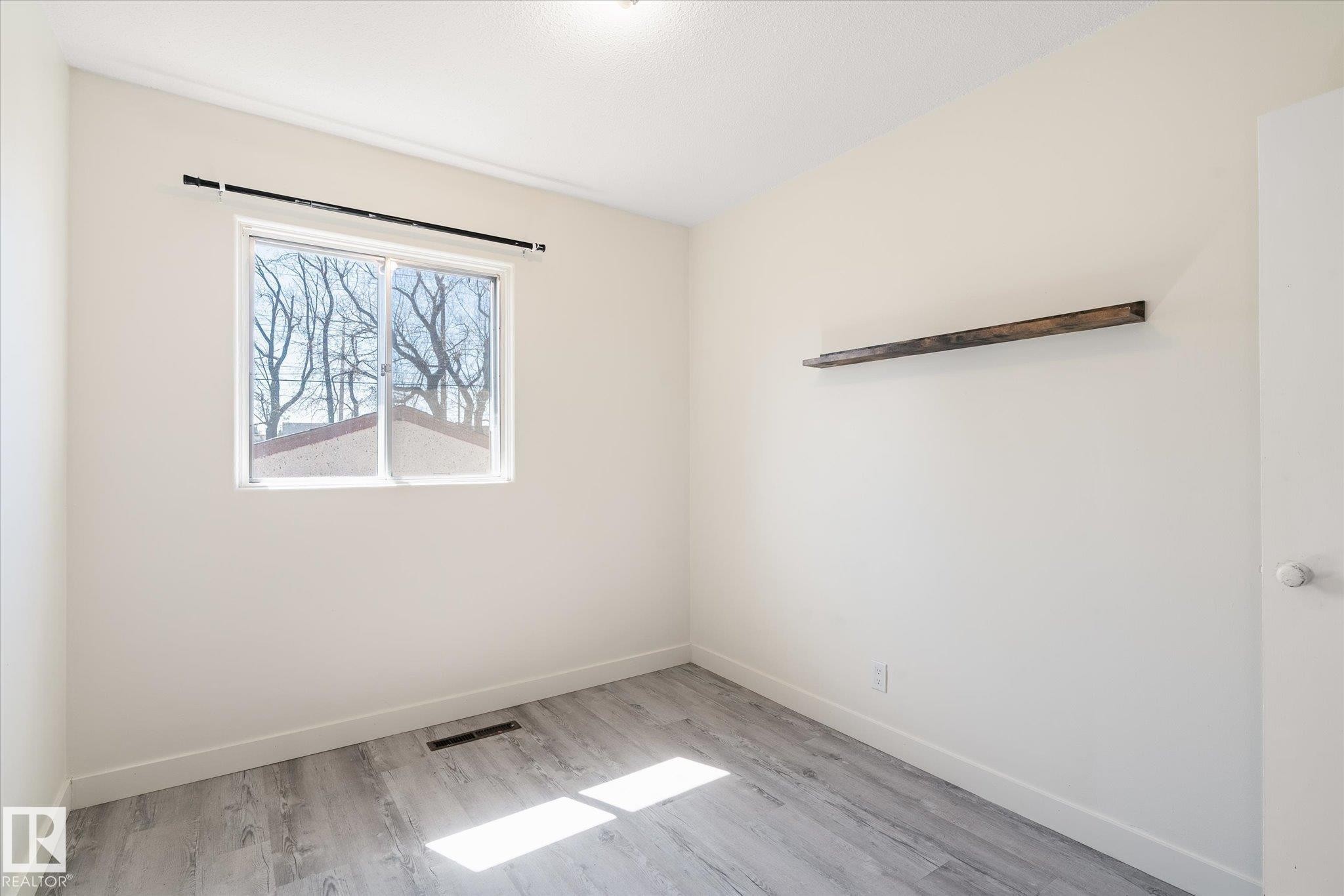 Room featuring light-toned walls, a single window with a black curtain rod, and wood-finish flooring - 10531 128 Avenue, Edmonton, AB - Indoor Photo Showing Other Room