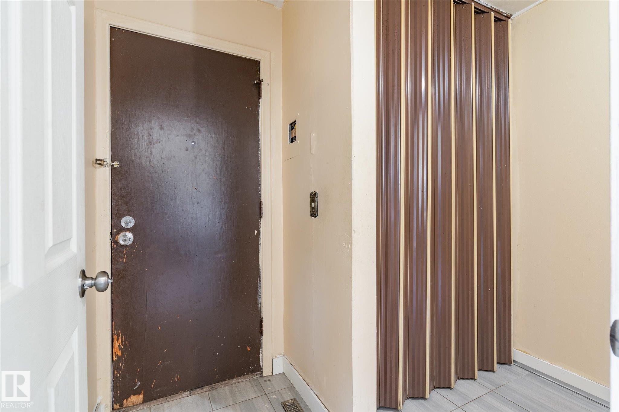 Entryway featuring a dark paneled door with a deadbolt, a light-colored interior door, a bi-fold closure, and light-toned floor tiling - 10531 128 Avenue, Edmonton, AB - Indoor Photo Showing Other Room