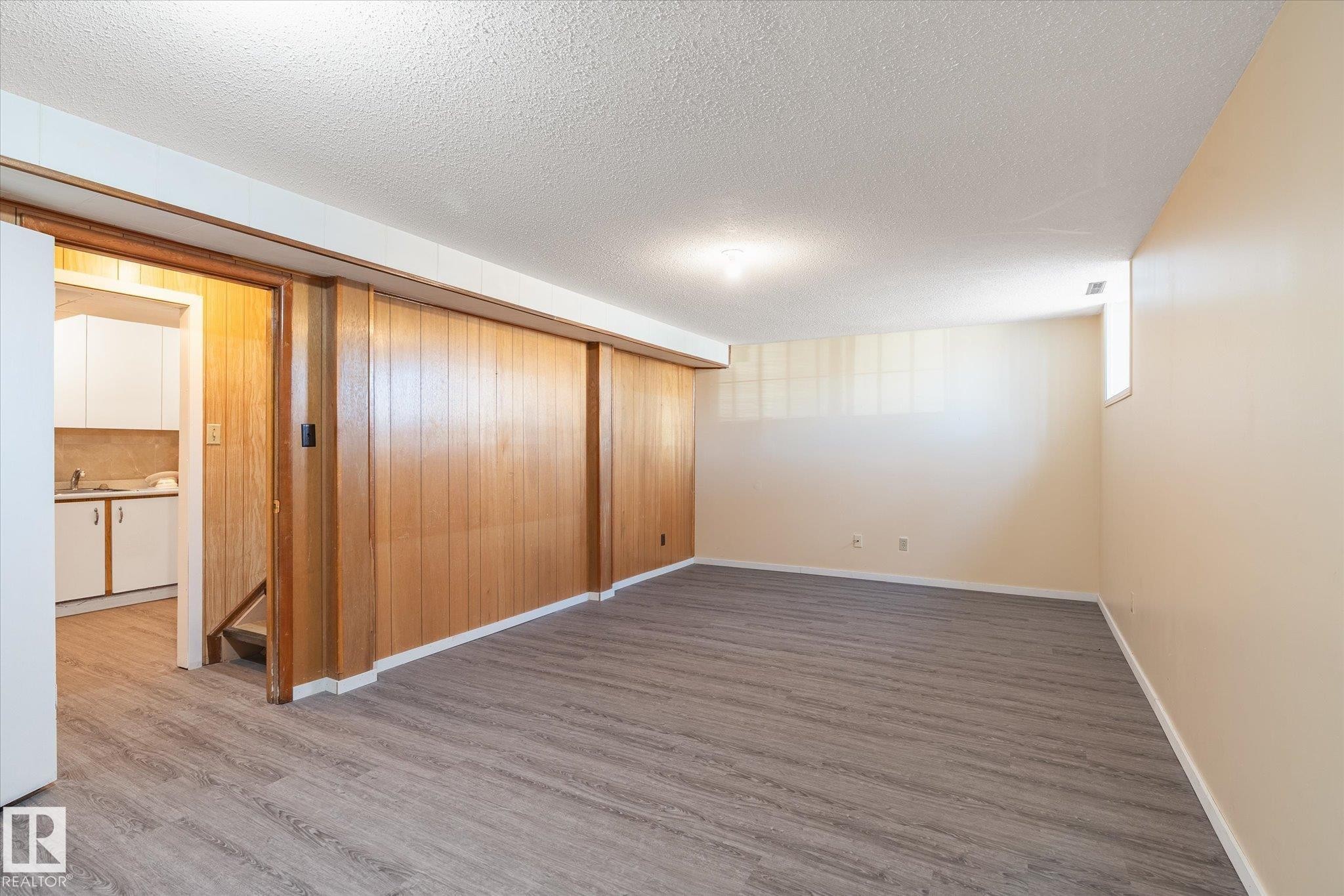 Spacious lower-level room featuring wood-finish paneling, light-toned walls, and wood-finish flooring - 10531 128 Avenue, Edmonton, AB - Indoor Photo Showing Other Room