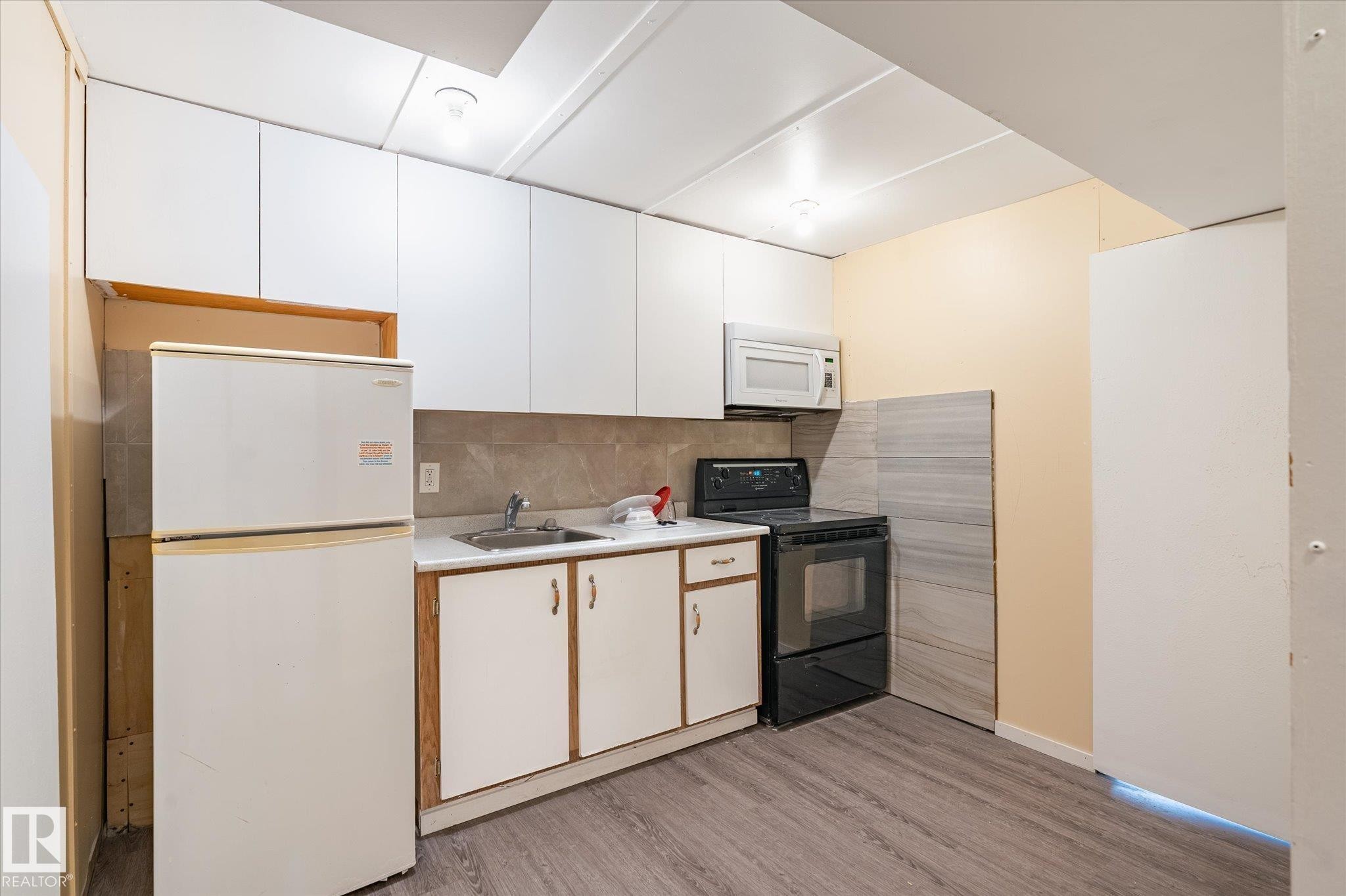 Kitchen featuring white upper cabinetry, a stainless steel sink, wood-finish flooring, a built-in microwave, and an electric range - 10531 128 Avenue, Edmonton, AB - Indoor Photo Showing Kitchen