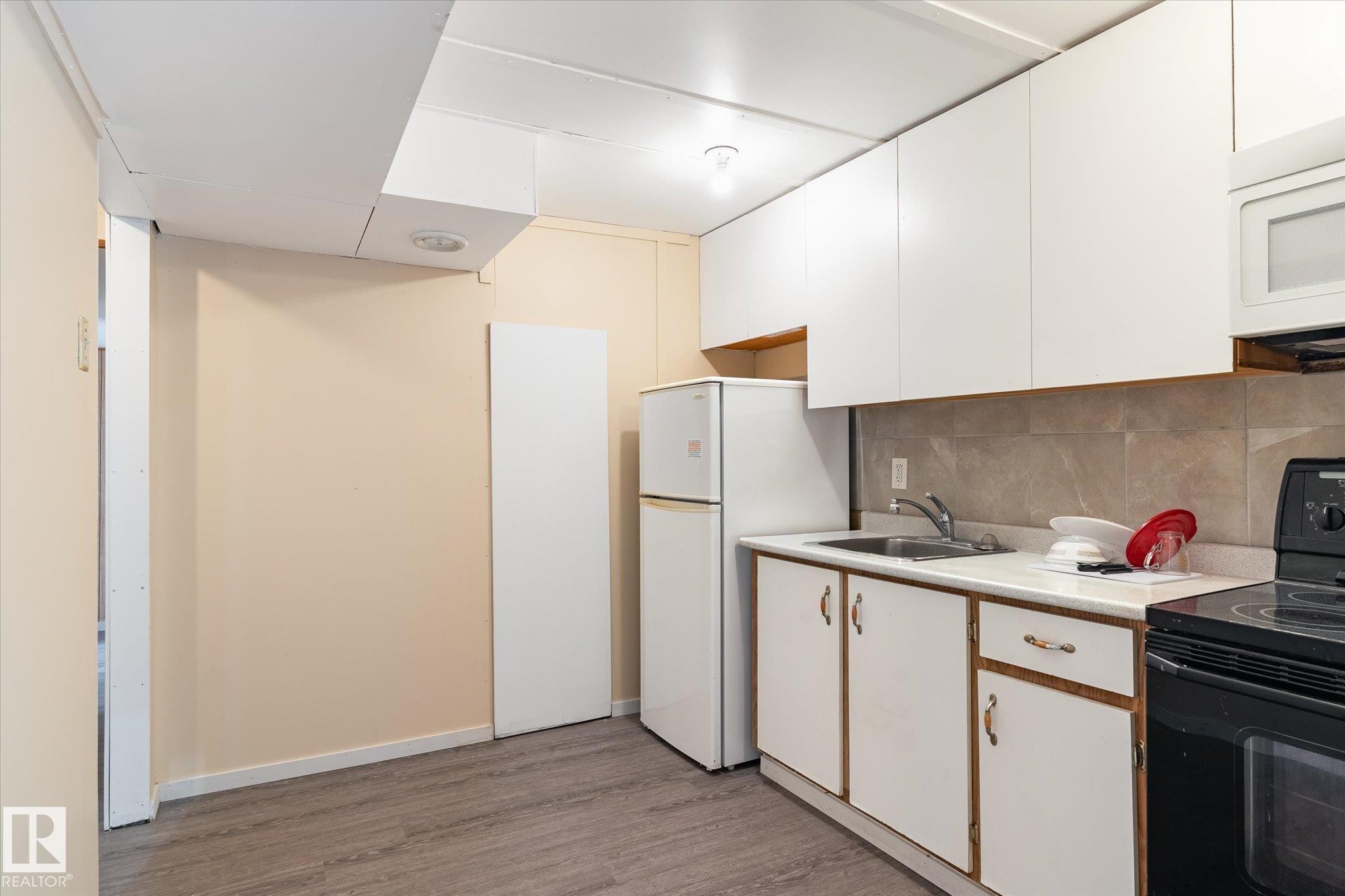 Kitchen area featuring white cabinetry, a double-door refrigerator, and a black electric range - 10531 128 Avenue, Edmonton, AB - Indoor Photo Showing Kitchen