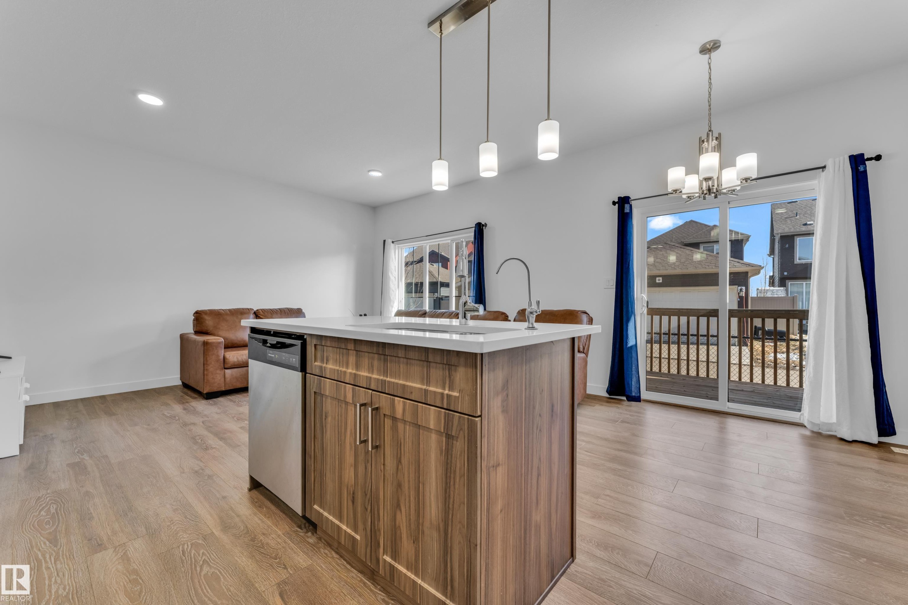 Central kitchen island with wood-finish cabinetry, white countertop, and integrated stainless steel dishwasher - 41 603 Orchards Boulevard, Edmonton, AB - Indoor Photo Showing Kitchen