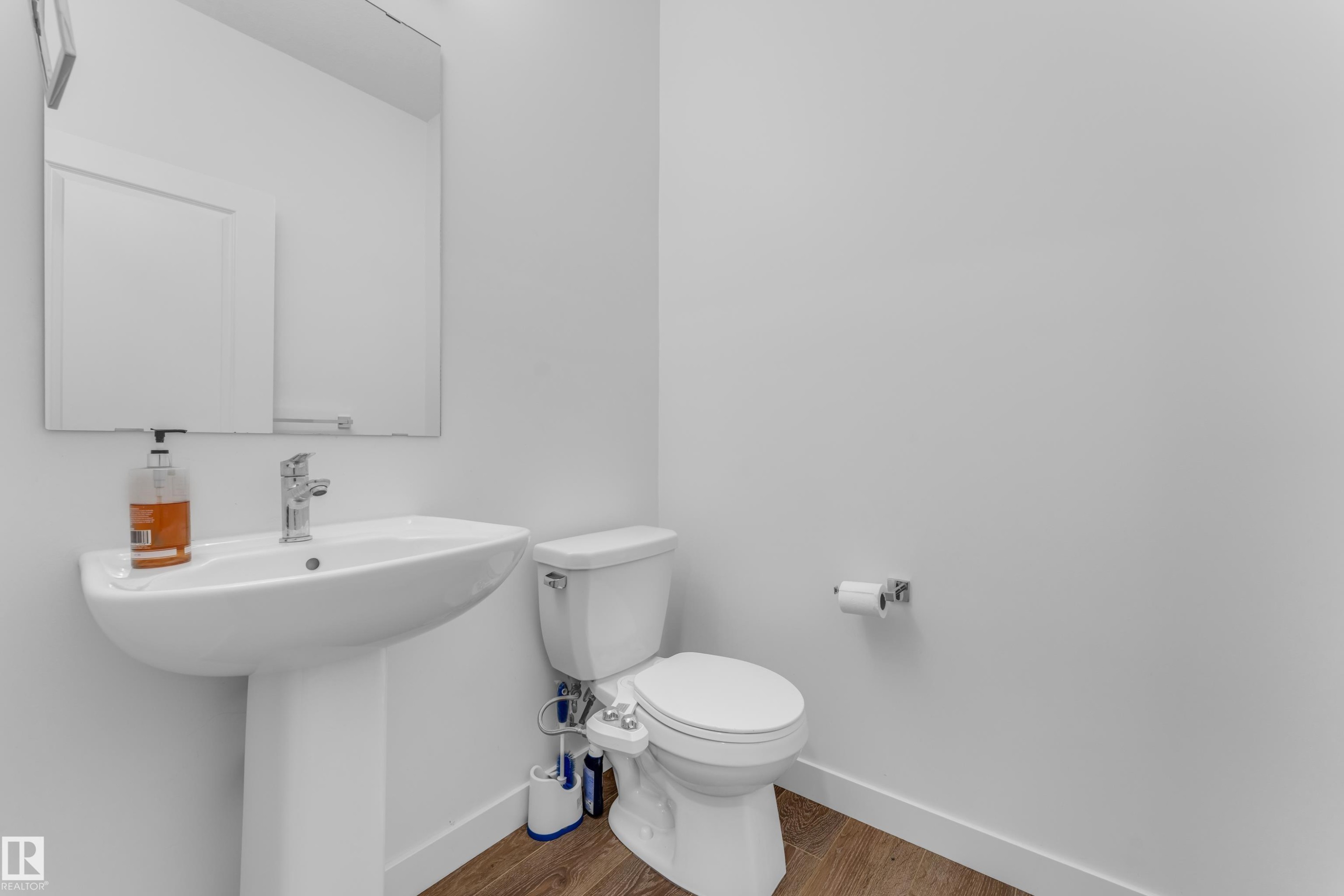 Bathroom featuring a pedestal sink, wall-mounted mirror, and wood-finish flooring - 41 603 Orchards Boulevard, Edmonton, AB - Indoor Photo Showing Bathroom