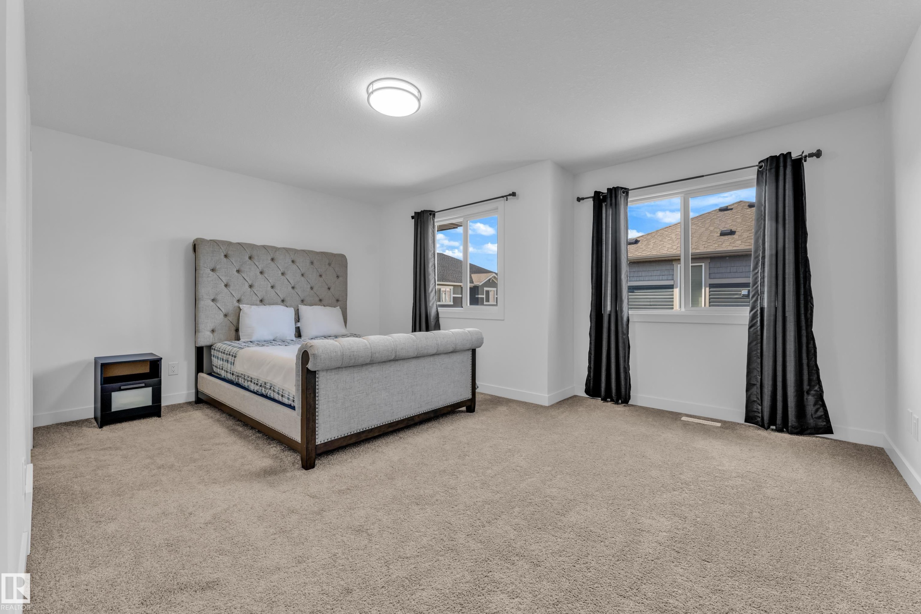 Spacious bedroom featuring light-colored carpeting, white walls, and a contemporary flush-mount ceiling light - 41 603 Orchards Boulevard, Edmonton, AB - Indoor