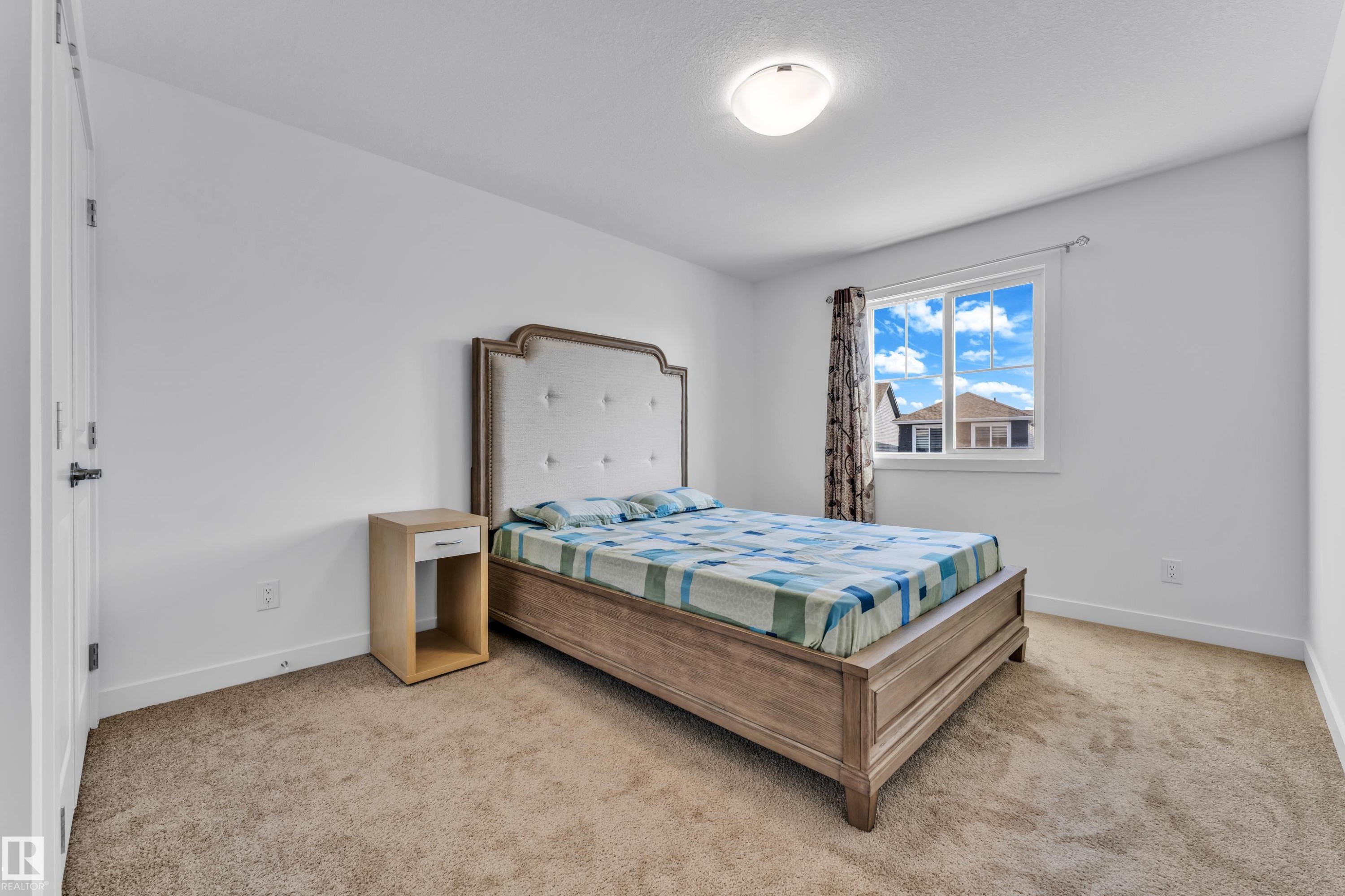 Bright bedroom featuring neutral carpeting, white walls, and a single window with curtain rods - 41 603 Orchards Boulevard, Edmonton, AB - Indoor Photo Showing Bedroom