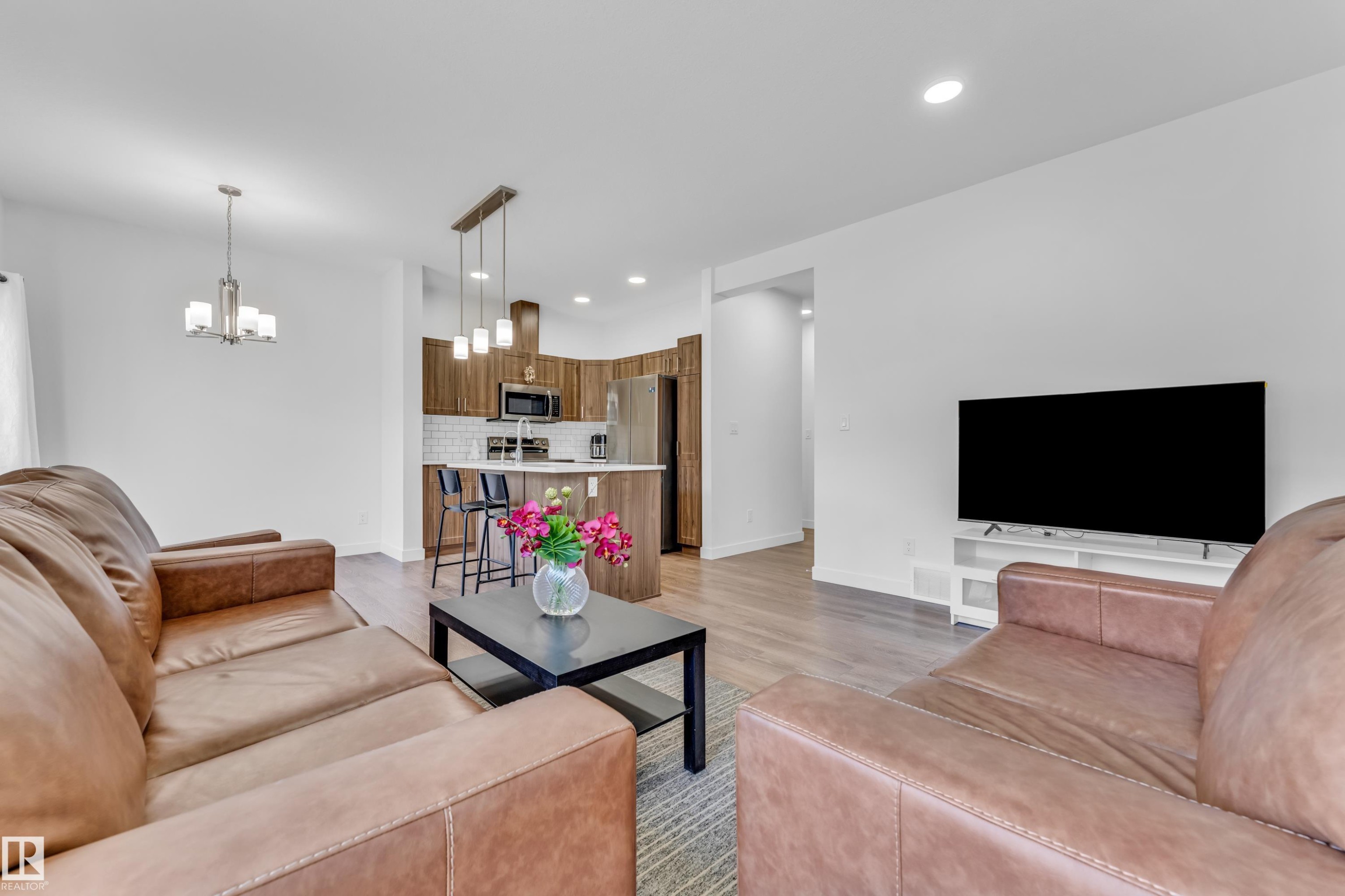 Open-concept living space featuring wood-finish flooring, recessed lighting, and a kitchen with stainless steel appliances, a white subway tile backsplash, and an island with pendant lighting - 41 603 Orchards Boulevard, Edmonton, AB - Indoor Photo Showing Living Room
