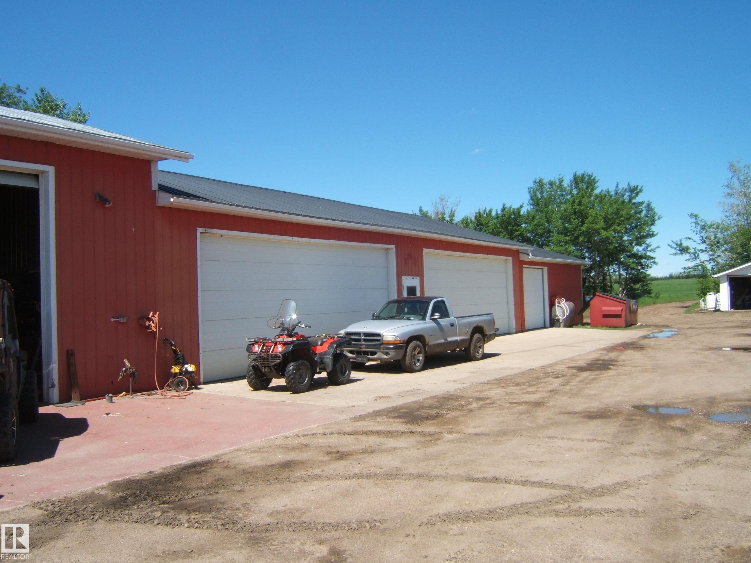 Red exterior building with two white garage doors, a white service door, and a black metal roof - 123064 Hwy 45, Rural Two Hills County, AB