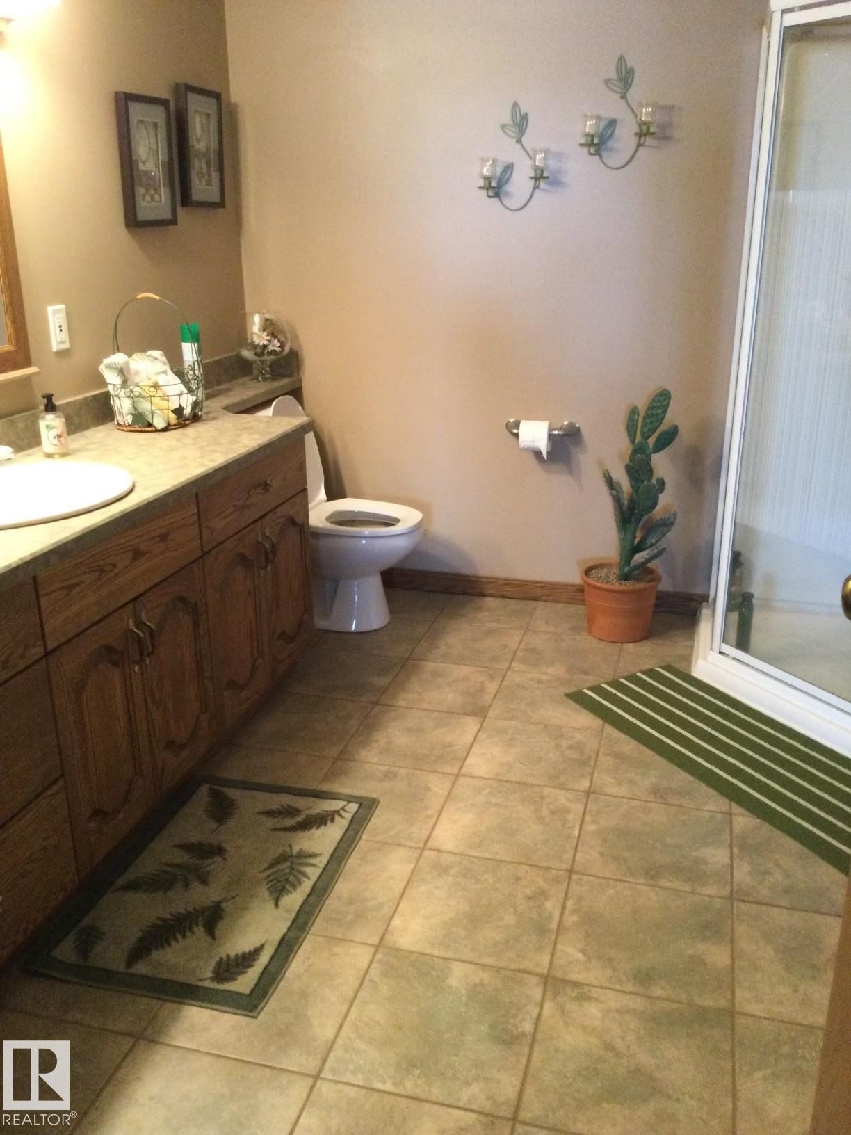 Bathroom featuring a spacious wood-finish vanity with an integrated sink, ample countertop space, a toilet, and a stand-up shower enclosure - 123064 Hwy 45, Rural Two Hills County, AB