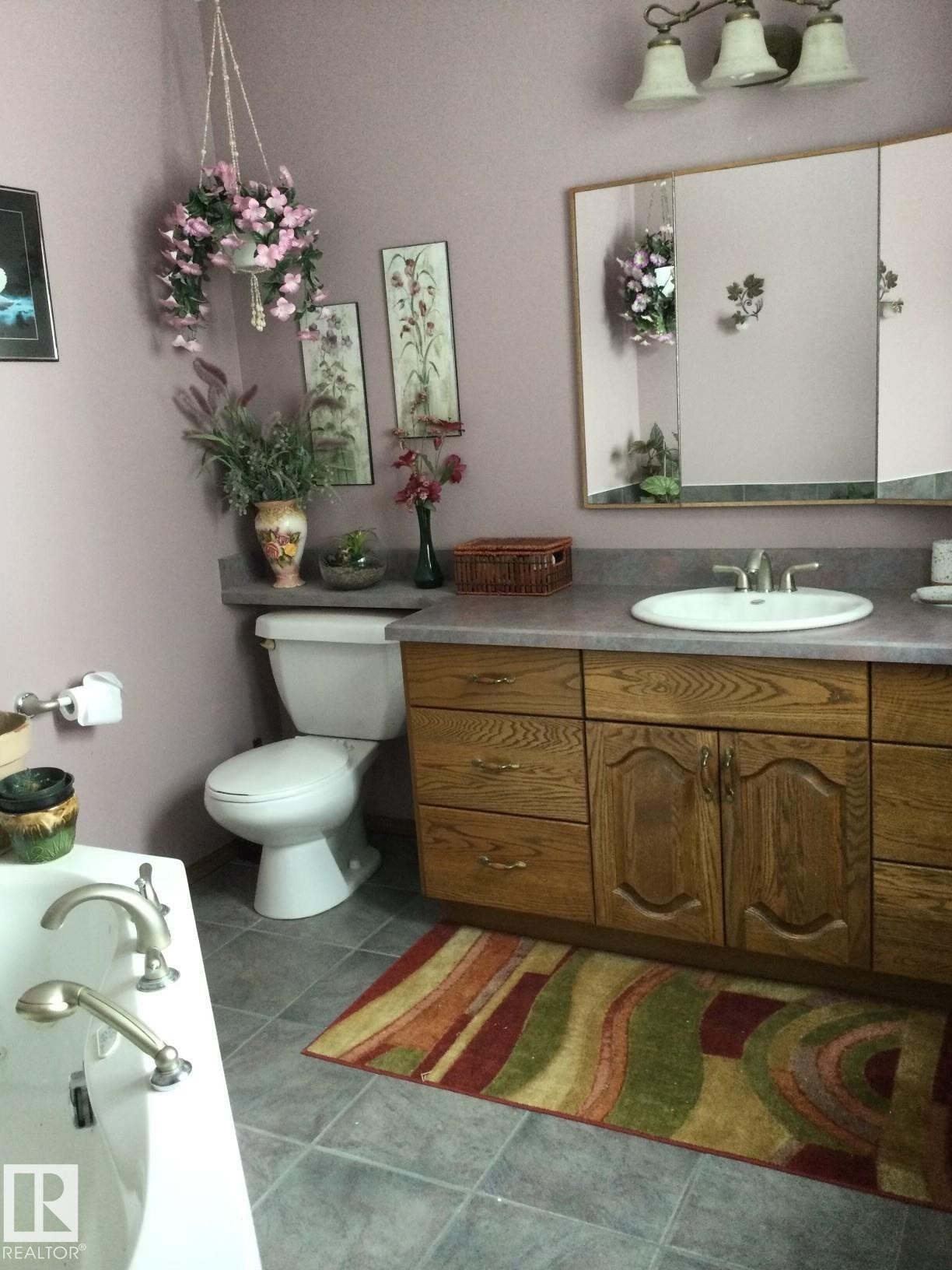 Bathroom featuring a light-colored vanity with a built-in sink, a wall-mounted mirror, and a three-light fixture overhead - 123064 Hwy 45, Rural Two Hills County, AB