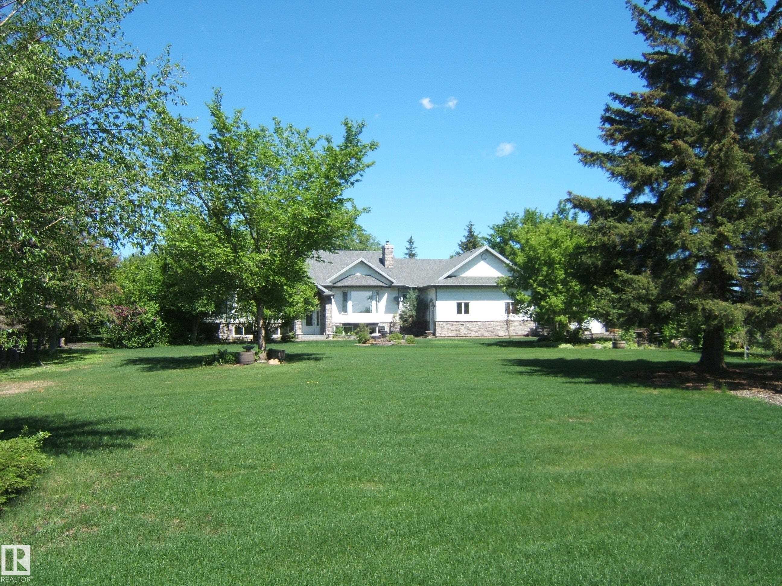 Expansive front lawn leading to a residence featuring a light-colored exterior with stone accents, multiple gables, and a prominent bay window - 123064 Hwy 45, Rural Two Hills County, AB