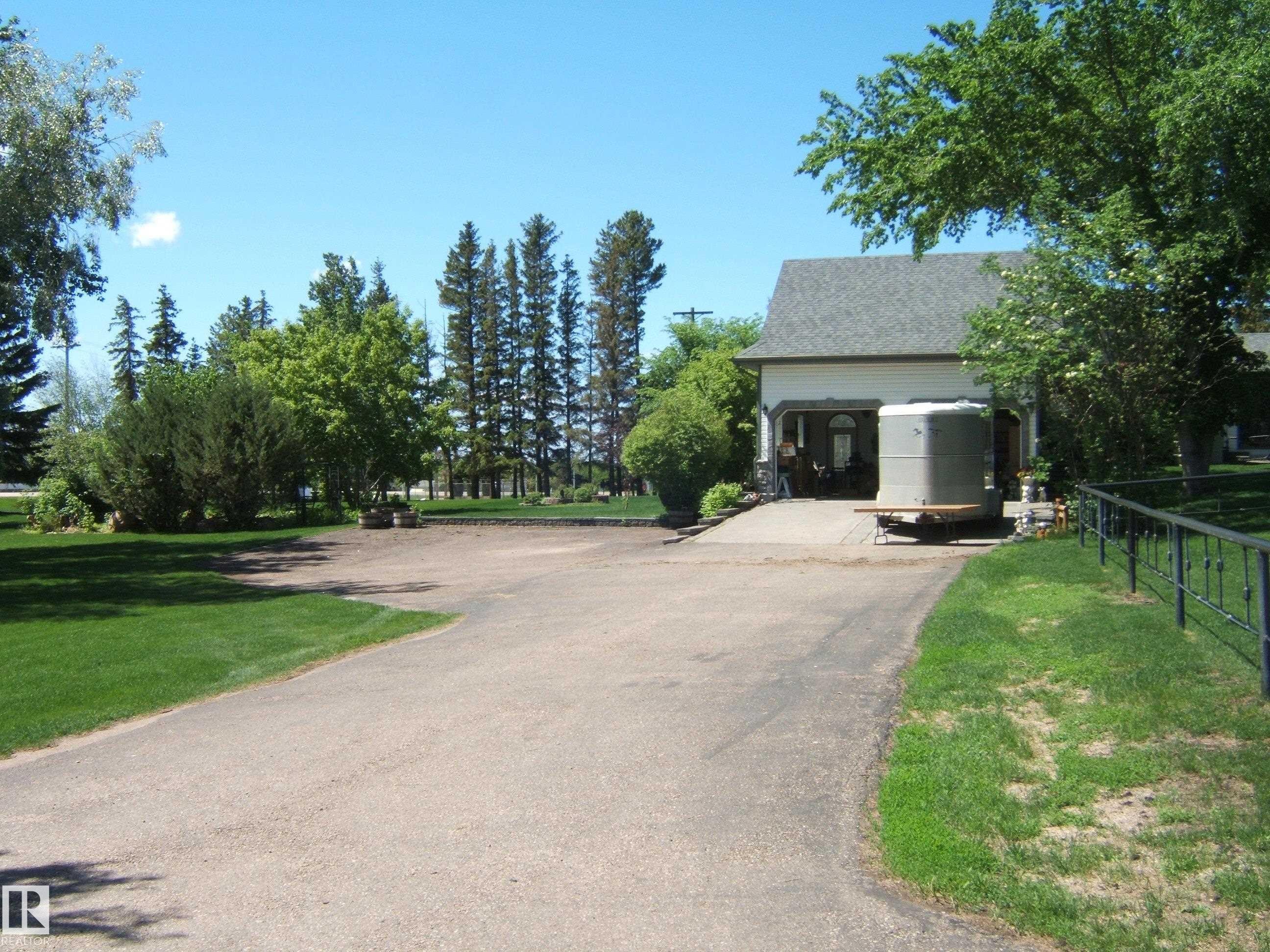 Asphalt driveway leading to a residence with a light-colored stucco exterior and a dark shingled roof - 123064 Hwy 45, Rural Two Hills County, AB