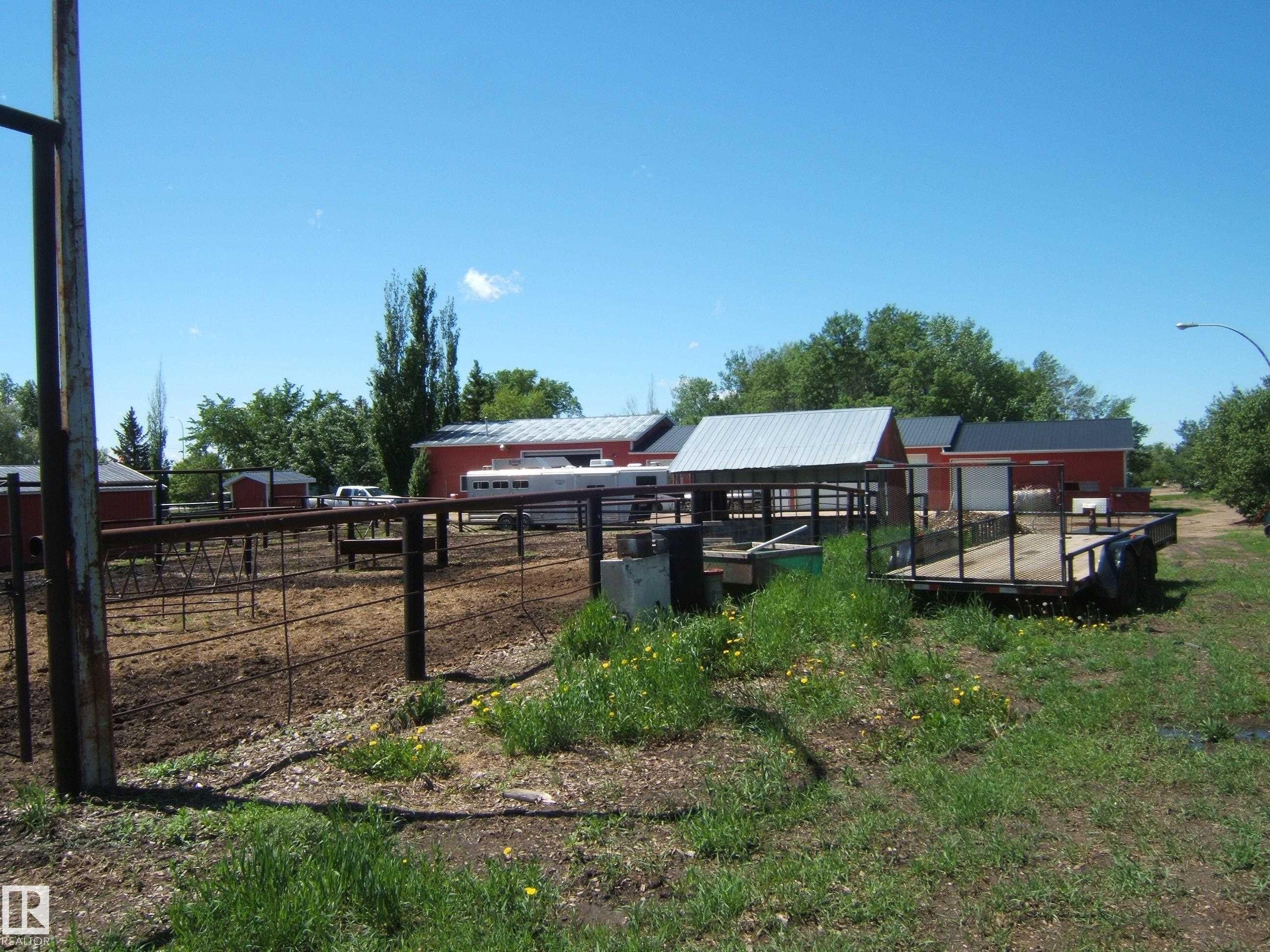 Agricultural property featuring multiple red outbuildings with metal roofs, fenced corrals, and established perimeter trees - 123064 Hwy 45, Rural Two Hills County, AB